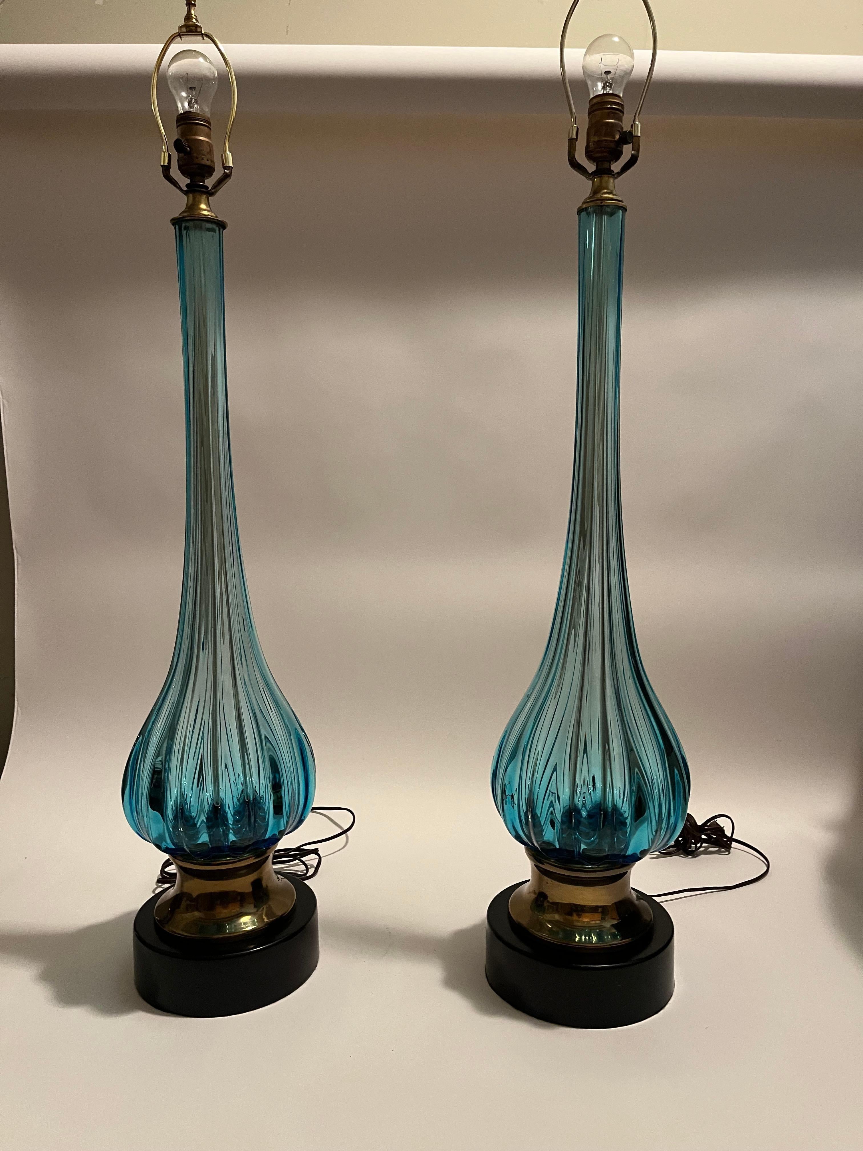 A pair of hand blown Murano ocean blue glass table lamps designed by Archimede Seguso and retailed by The Marbro Lamp Co. Manufactured in the early 1960s, the graceful lamps are set upon gold and black base characteristic of the Marbro Lamp Co.