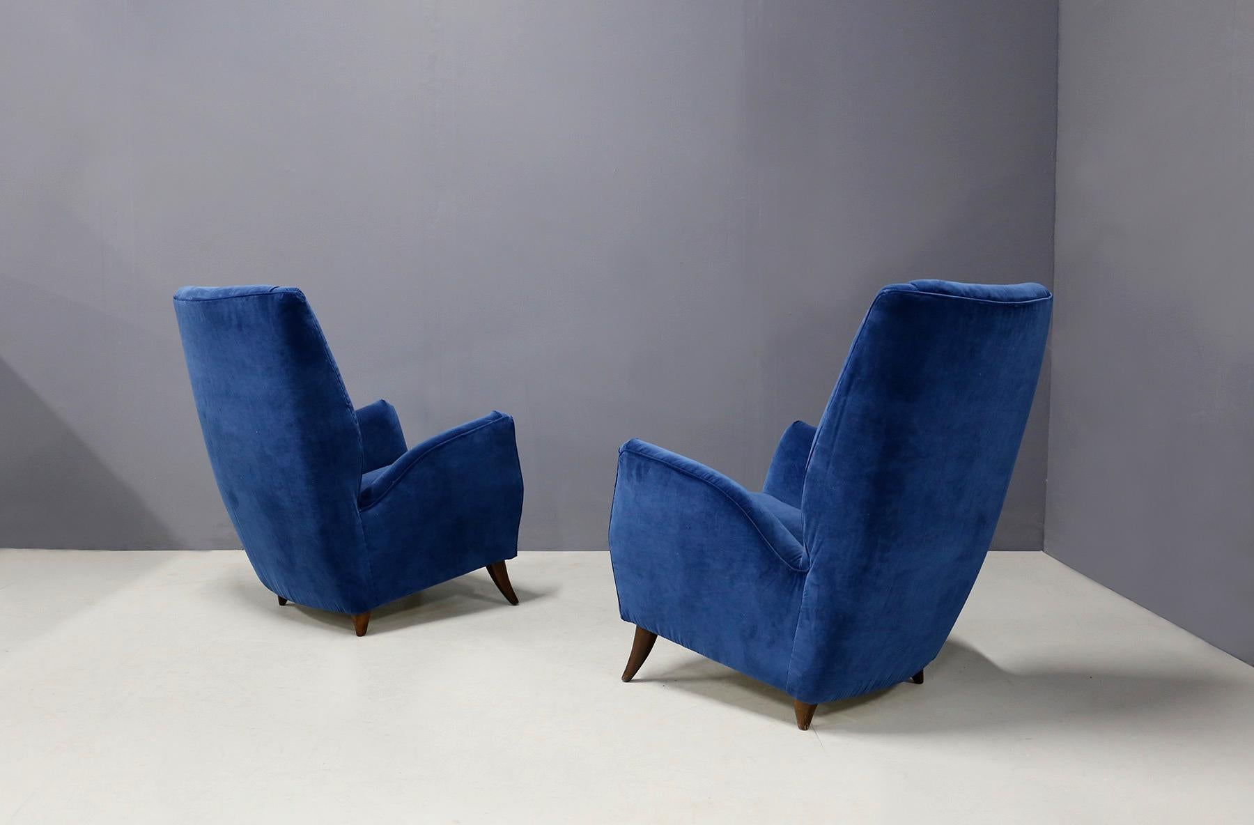 Pair of elegant armchairs attributed to designer Gio Ponti from 1950.
The armchairs have been re-lined in blue velvet. Note their armrests with high shape and high backrest, for greater comfort. Its wooden feet are cone-shaped. The armchairs are