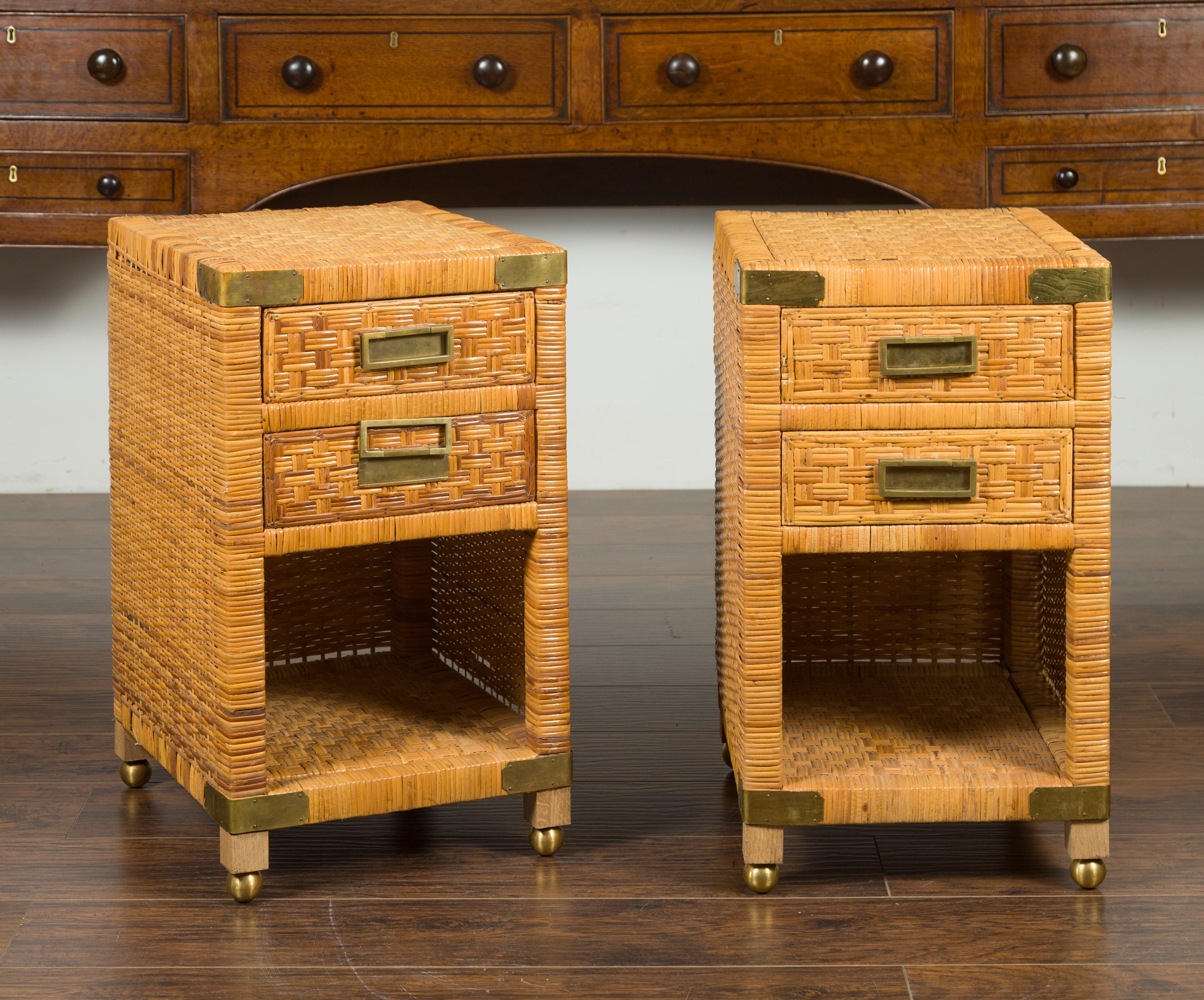 A vintage pair of Asian rattan bedside tables from the mid-20th century, with drawers and brass accents. Created during the mid-20th century, each of this pair of rattan bedside tables features a rectangular top sitting above two drawers, fitted