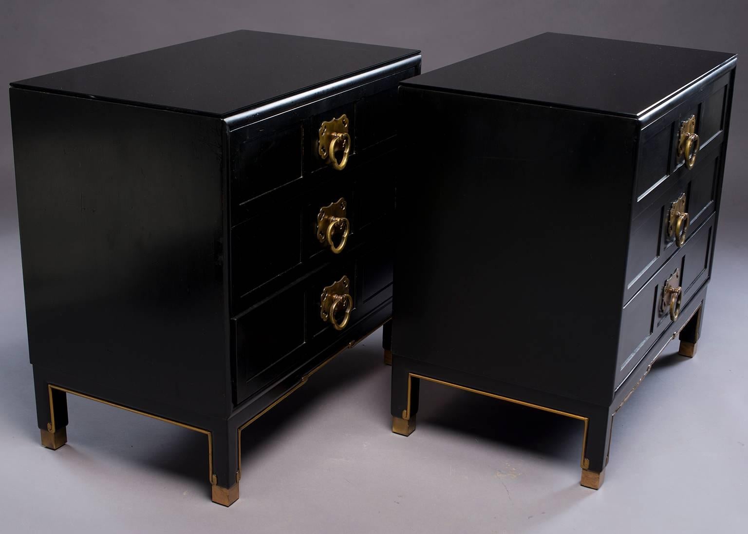 Pair of small three drawer chests with Asian styling. Black lacquer finish with original brass hardware, gilded details, brass foot caps and new custom glass tops. Tag from now defunct American manufacturer Treasure Chest Furniture from Zeeland, MI