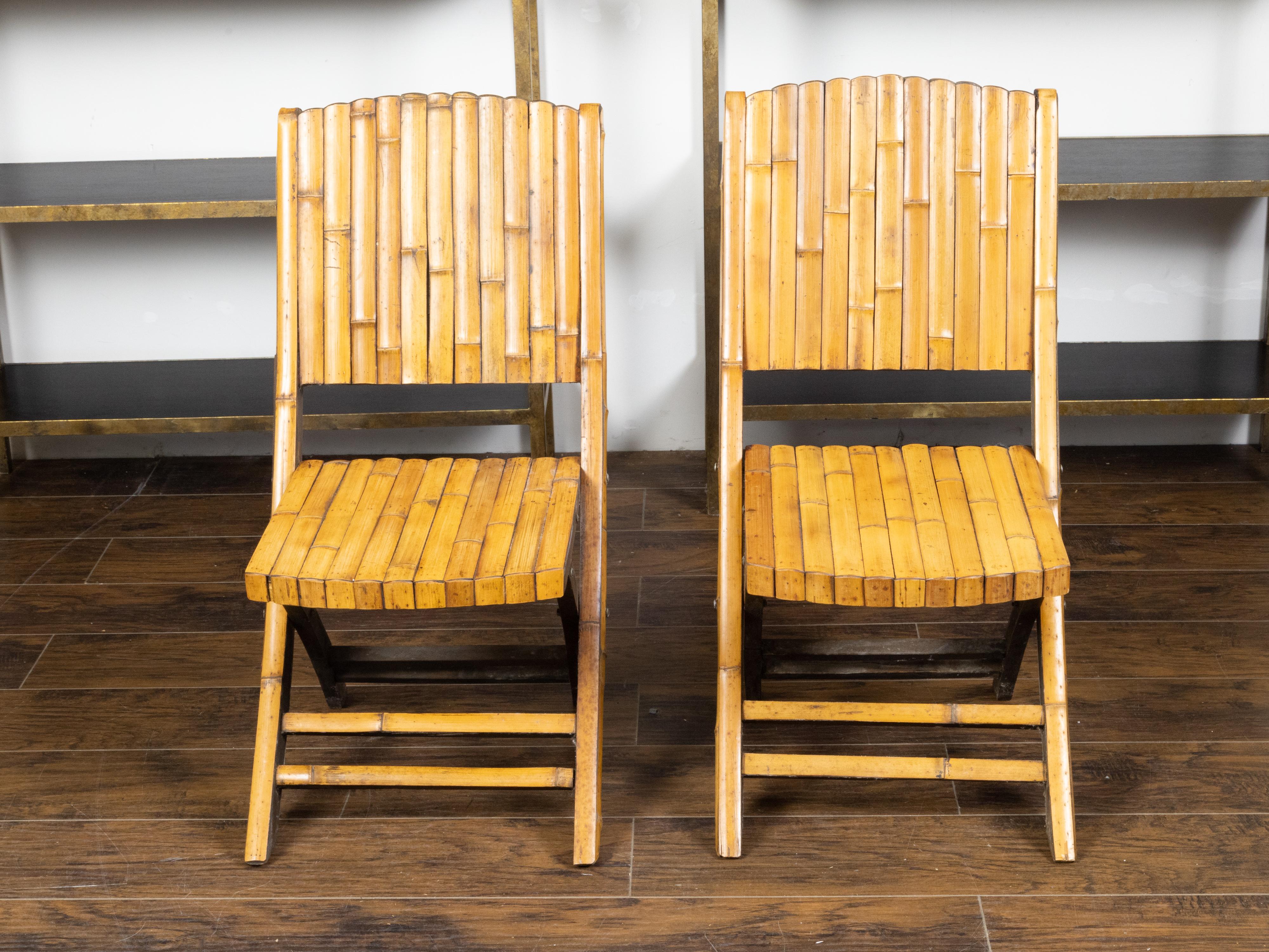 A pair of bamboo folding chairs from the mid 20th century, with light brown patina. Created during the midcentury period, each of this pair of folding chairs features a slatted bamboo structure perfectly complimented by a light colored patina.