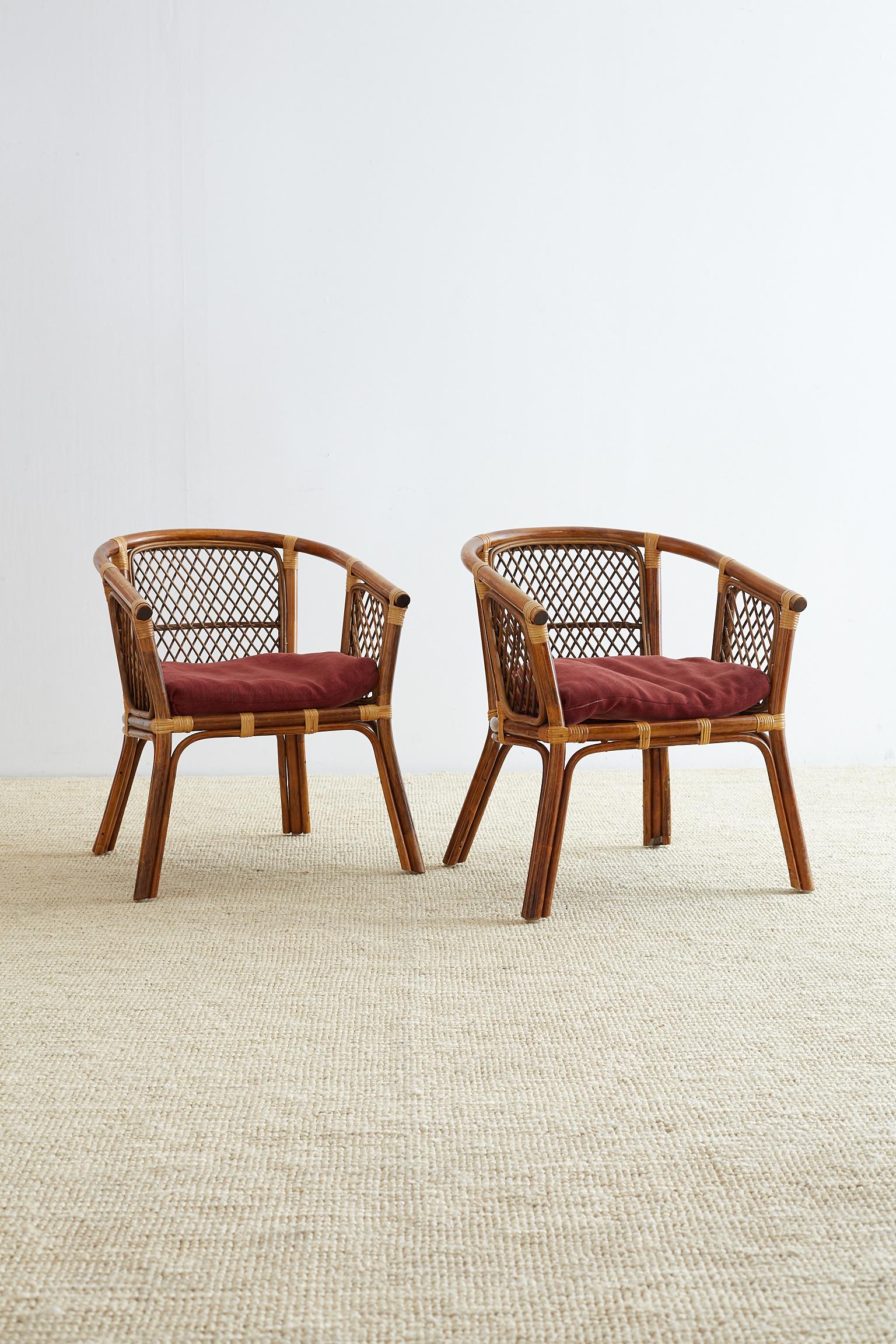 Stylish pair of Mid-Century Modern bamboo rattan club chairs featuring a barrel back design. The frames have decorative open lattice fretwork on the back and sides. The seat has an upholstered loose cushion with a vintage fabric. Good joinery