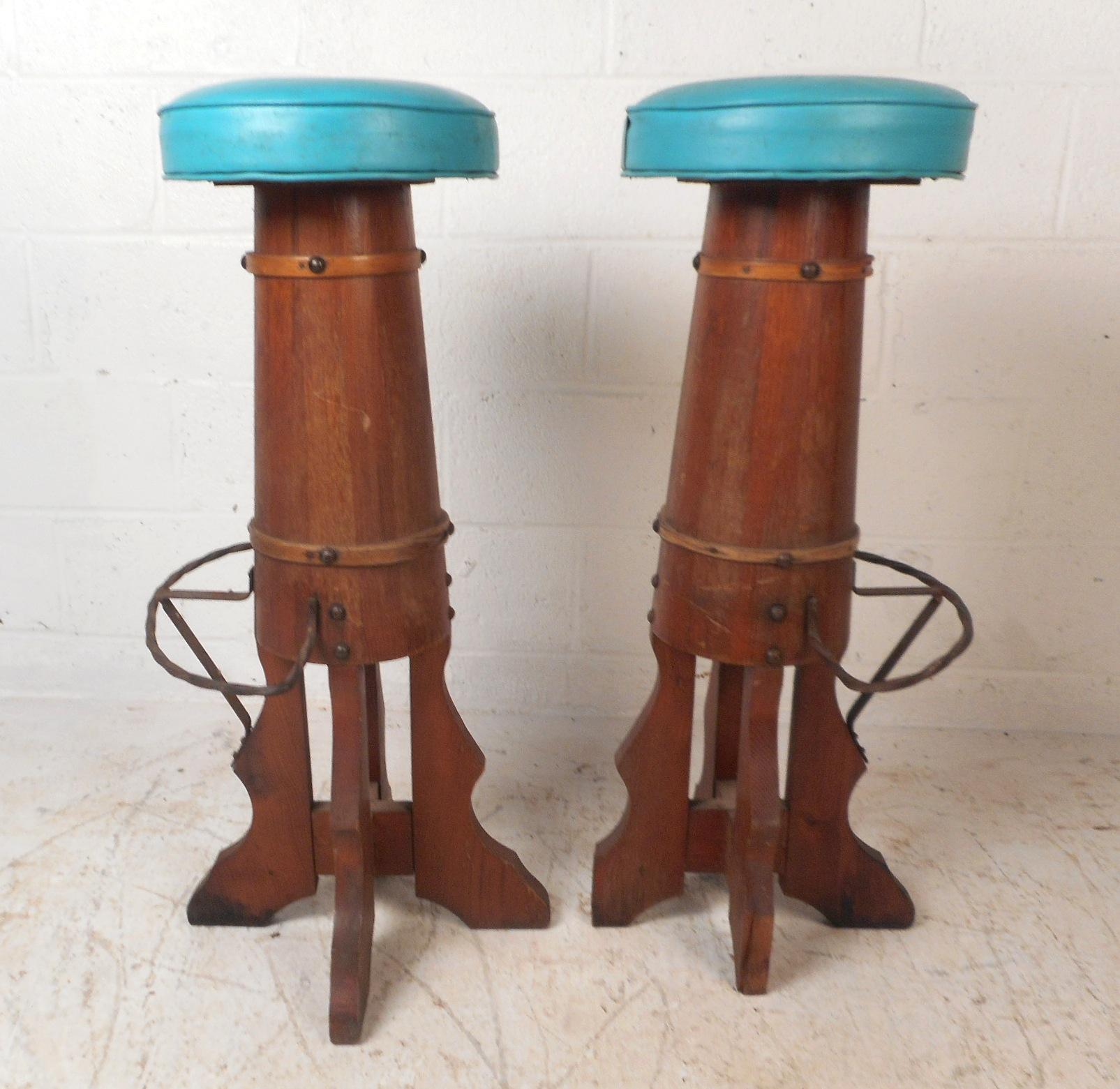 This beautiful pair of vintage modern bar stools feature a barrel style frame with unique spiral iron kick rests. The unusual design has carved feet and a teal blue vinyl covered seat giving off a smooth nautical vibe. This wonderful pair makes the
