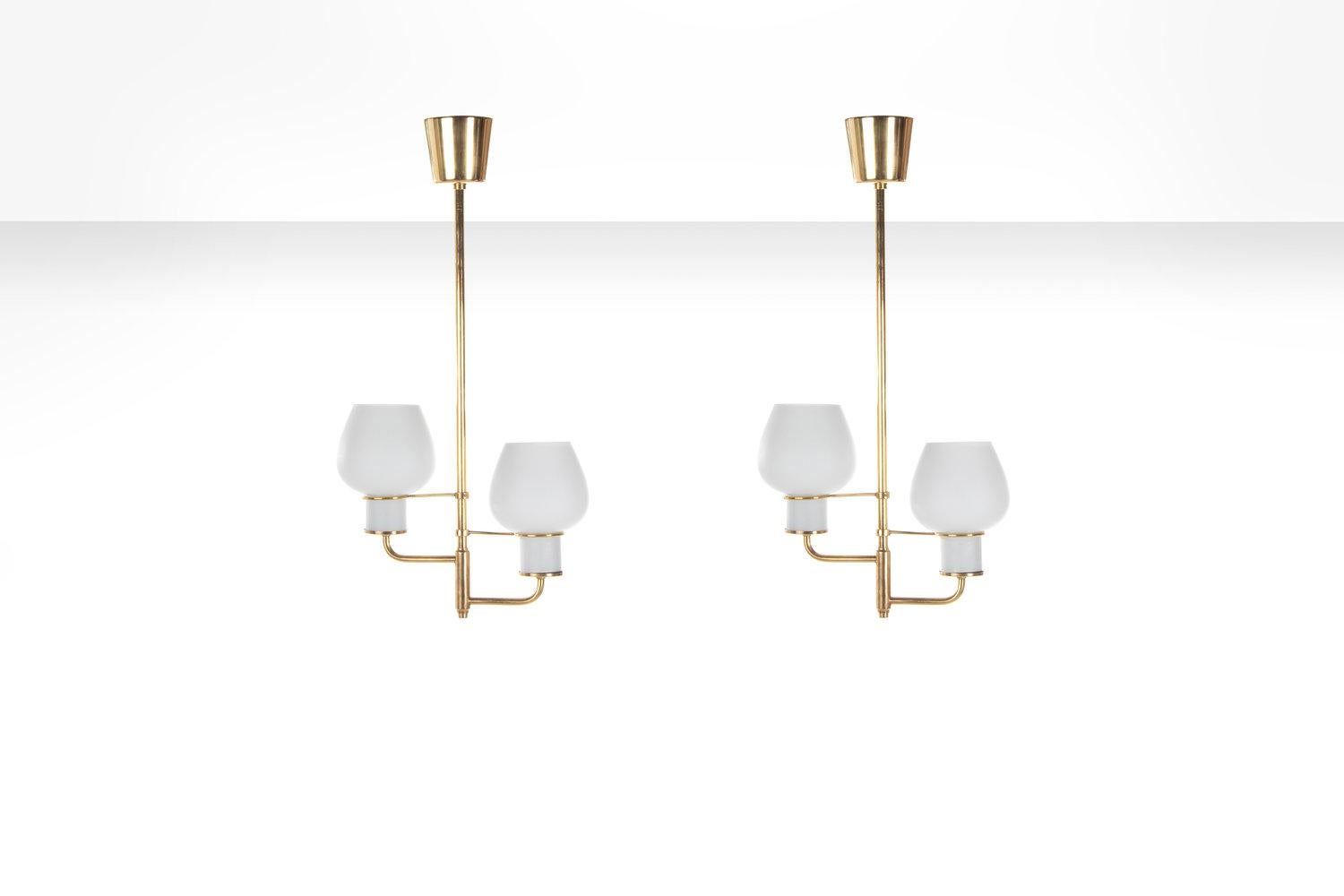 Two hand-blown, double opal glass shades with an organic shape, complimented by a beautiful brass body. The lamps are suspended by a firm stem, ending in a curvy brass canopy towards the ceiling. The neck of the shades is held by two additional