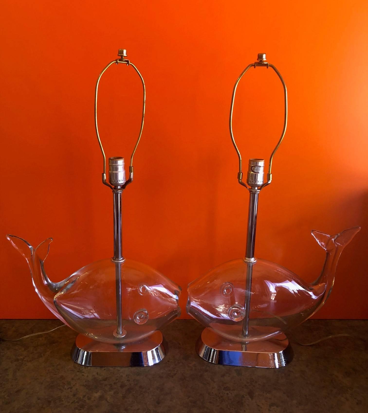Pair of midcentury glass fish lamps by Blenko, circa 1960s. The lamps are handblown clear glass fish mounted on a chrome base with a chrome stem and include two stitched rawhide lamp shades. The lamps are in very good vintage working condition with