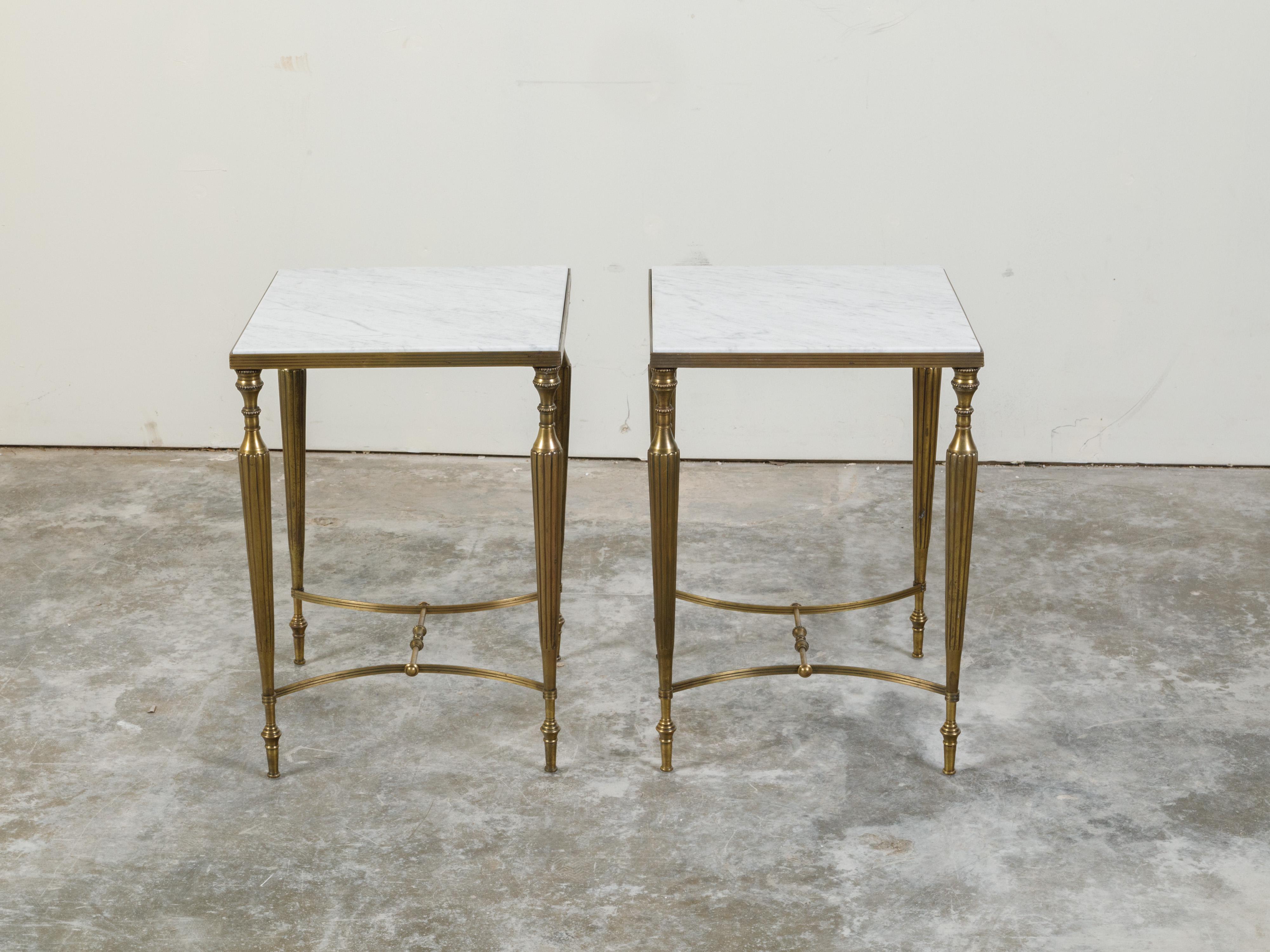 A pair of brass side tables from the mid 20th century, with white veined marble tops and curving H-form stretchers. Created during the midcentury period, each of this pair of brass side tables features a square white veined marble top secured within