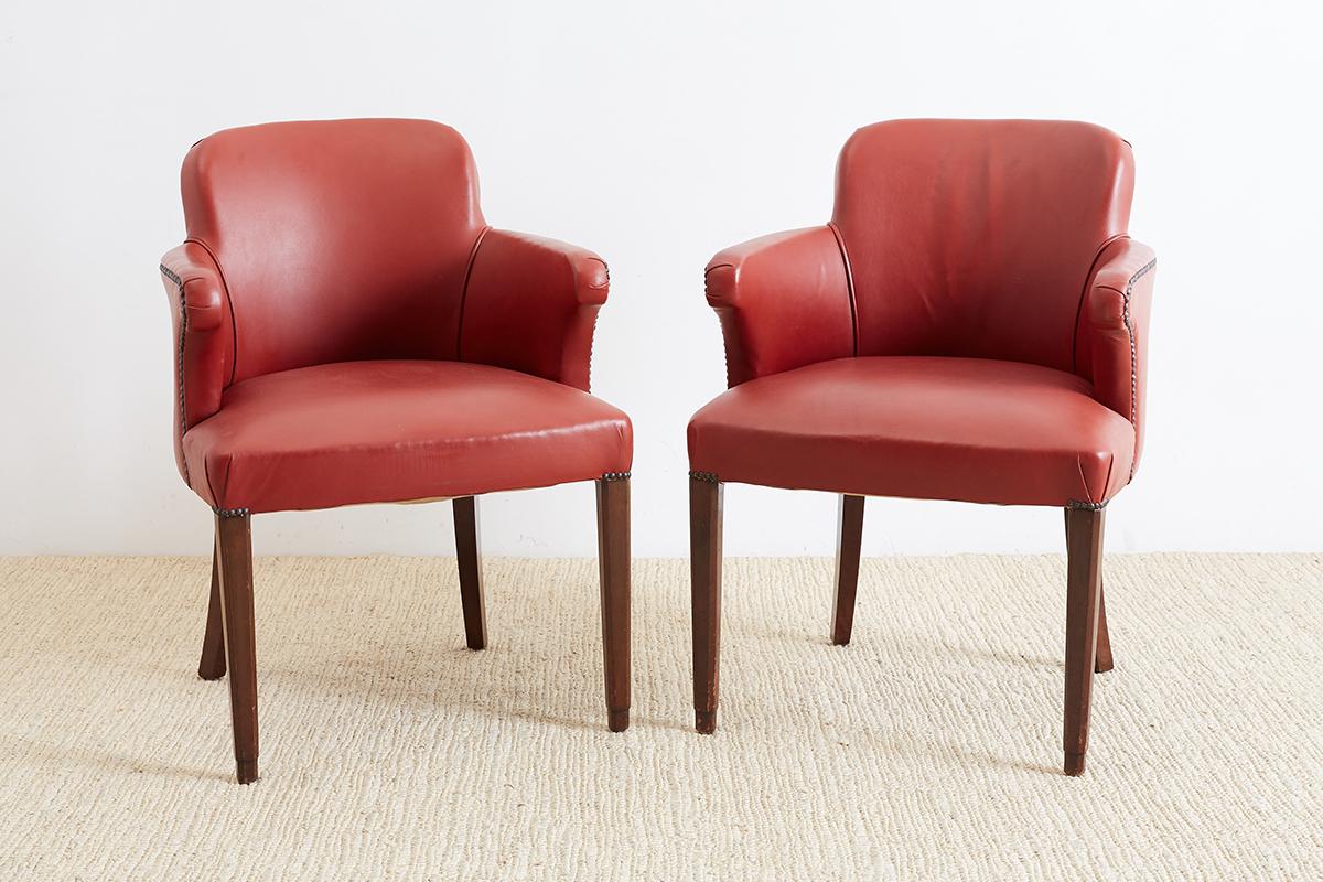 Distinctive pair of Mid-Century Modern brass studded leather armchairs finished in a rich brick red color. Unique shape and profile walnut frame with pointed arms. Bordered trim with brass tack nailheads. Very comfortable and fully padded with