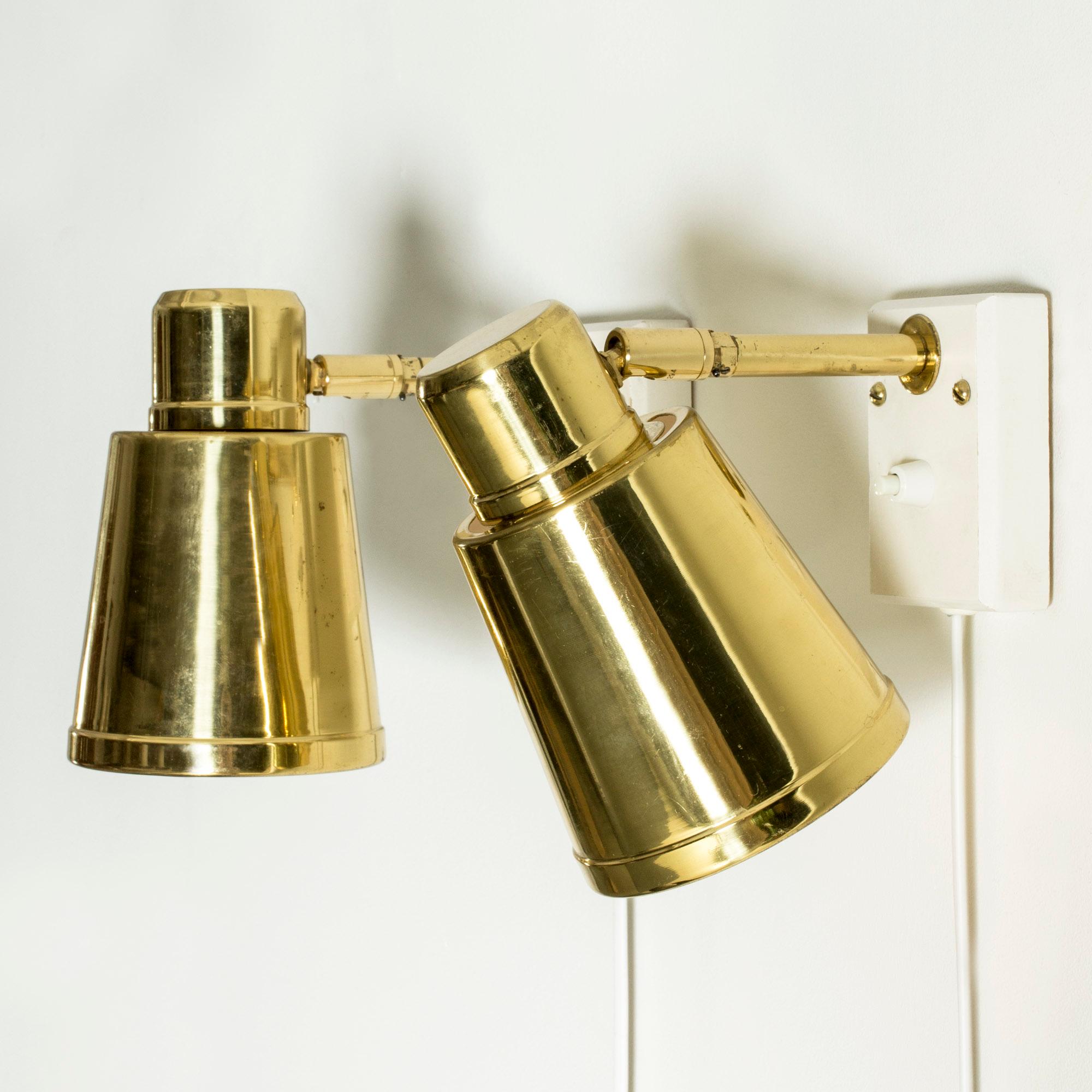 Pair of brass wall lamps from Bäcklunds Järn och Smide, mounted on white wooden wall mountings. Sleek design, angle adjustable inwards.