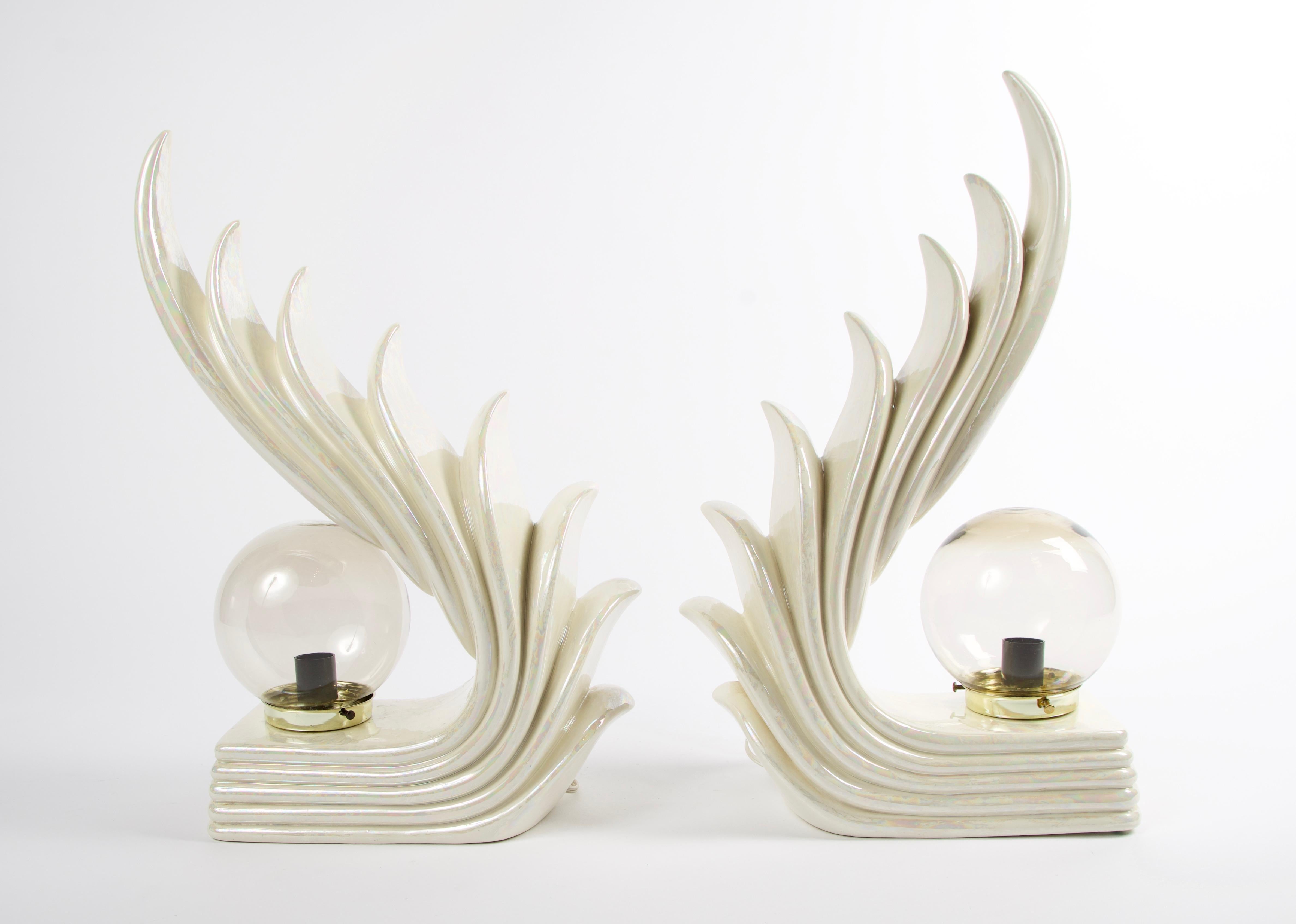 Stunning pair of Art Deco sculptural table lamps with a cascading wave design. These lamps have a cream ceramic glaze with an iridescent finish. The globes are a lightly smoked glass with a brass base. Due to them being handmade there are slight