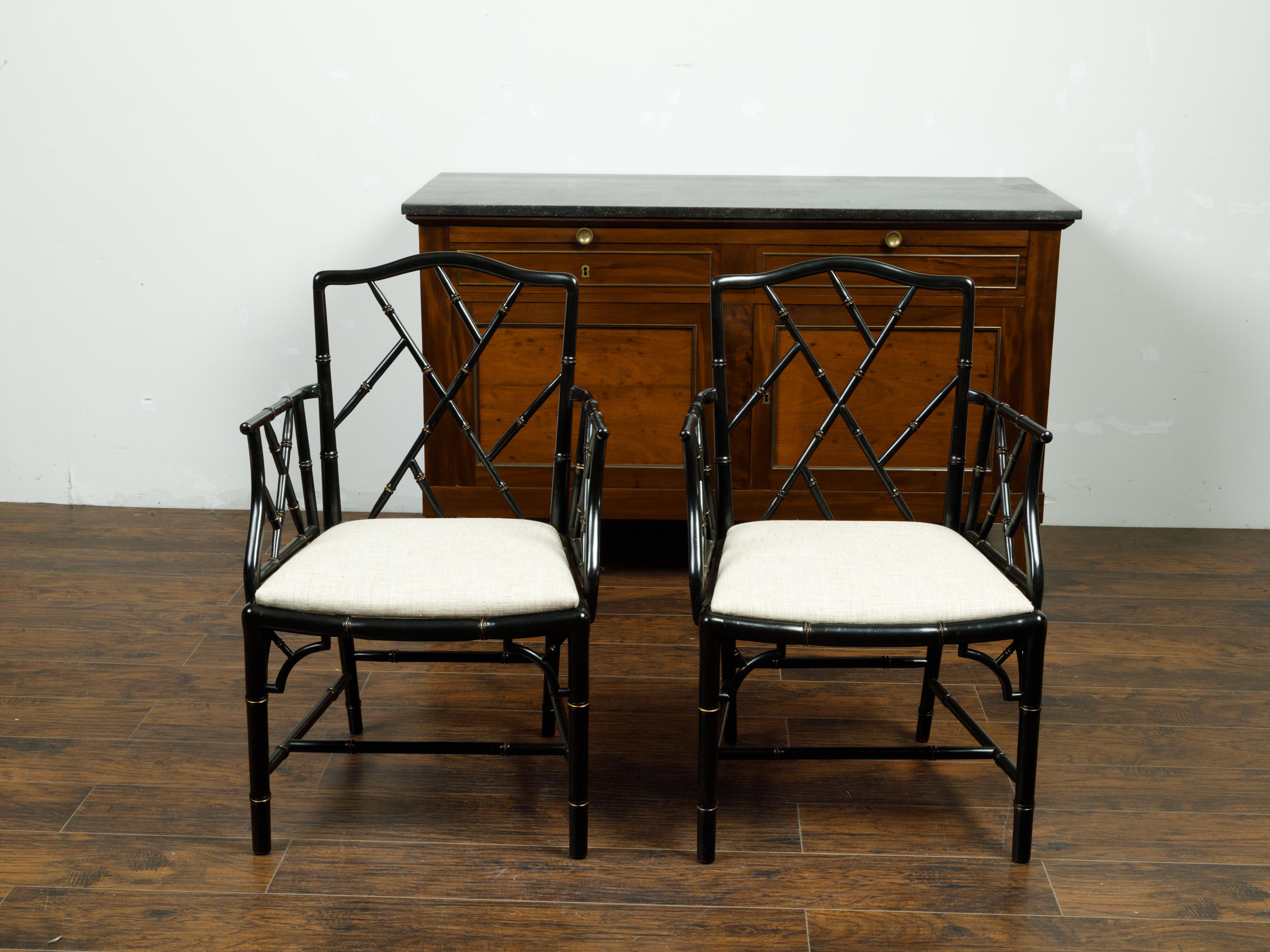 A pair of vintage Chinese Chippendale style black faux bamboo armchairs from the mid 20th century, with new upholstery. Made in the USA during the midcentury period, each of this pair of faux bamboo armchairs features a Chinese Chippendale ebonized