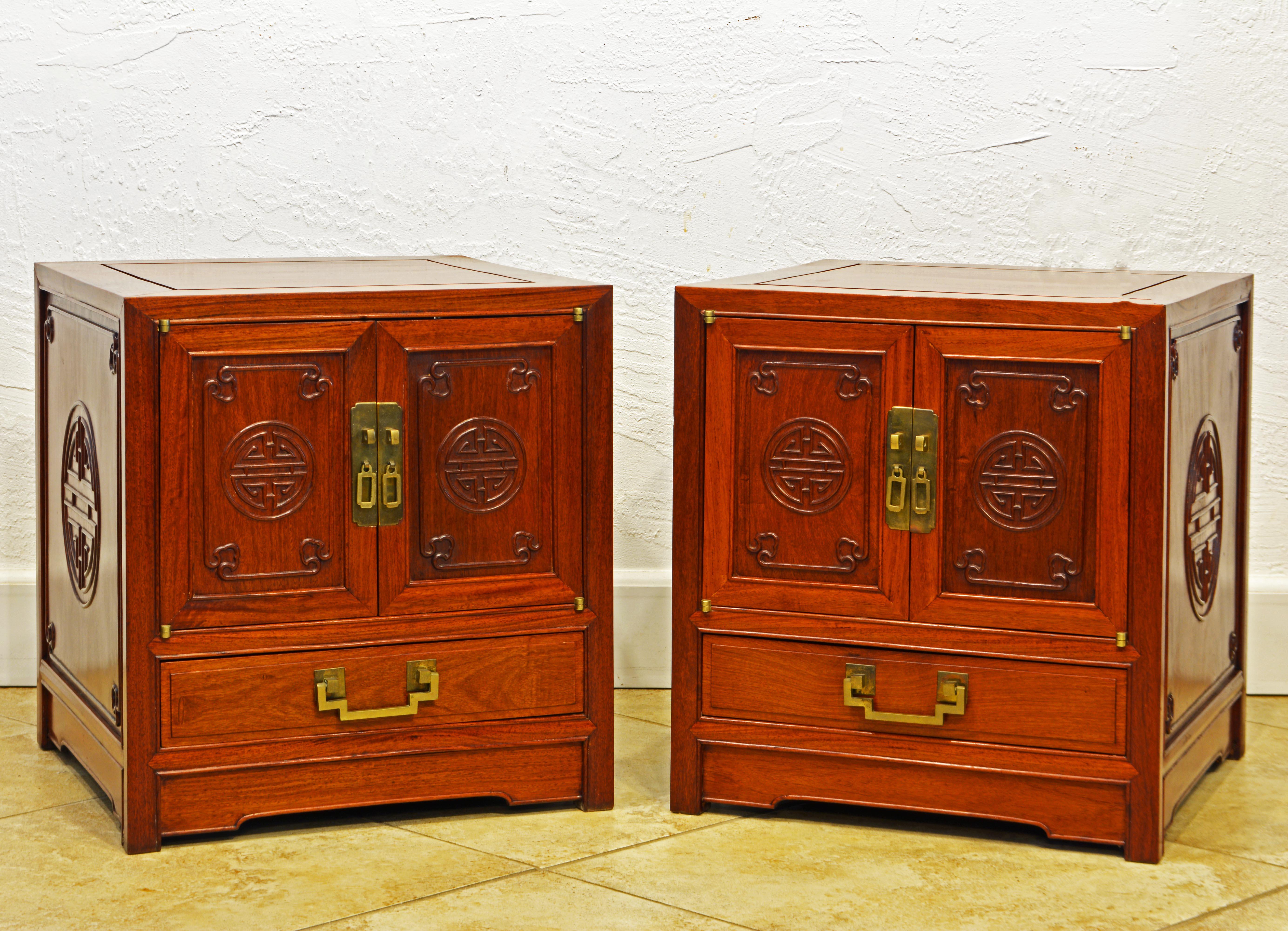 This fine pair of Chinese carved solid mahogany end tables and cabinets represent the great craftsmanship for which George Zee, Hong Kong, was widely known. Timeless elegance, warm color, detailed carvings and great hardware set them apart from the