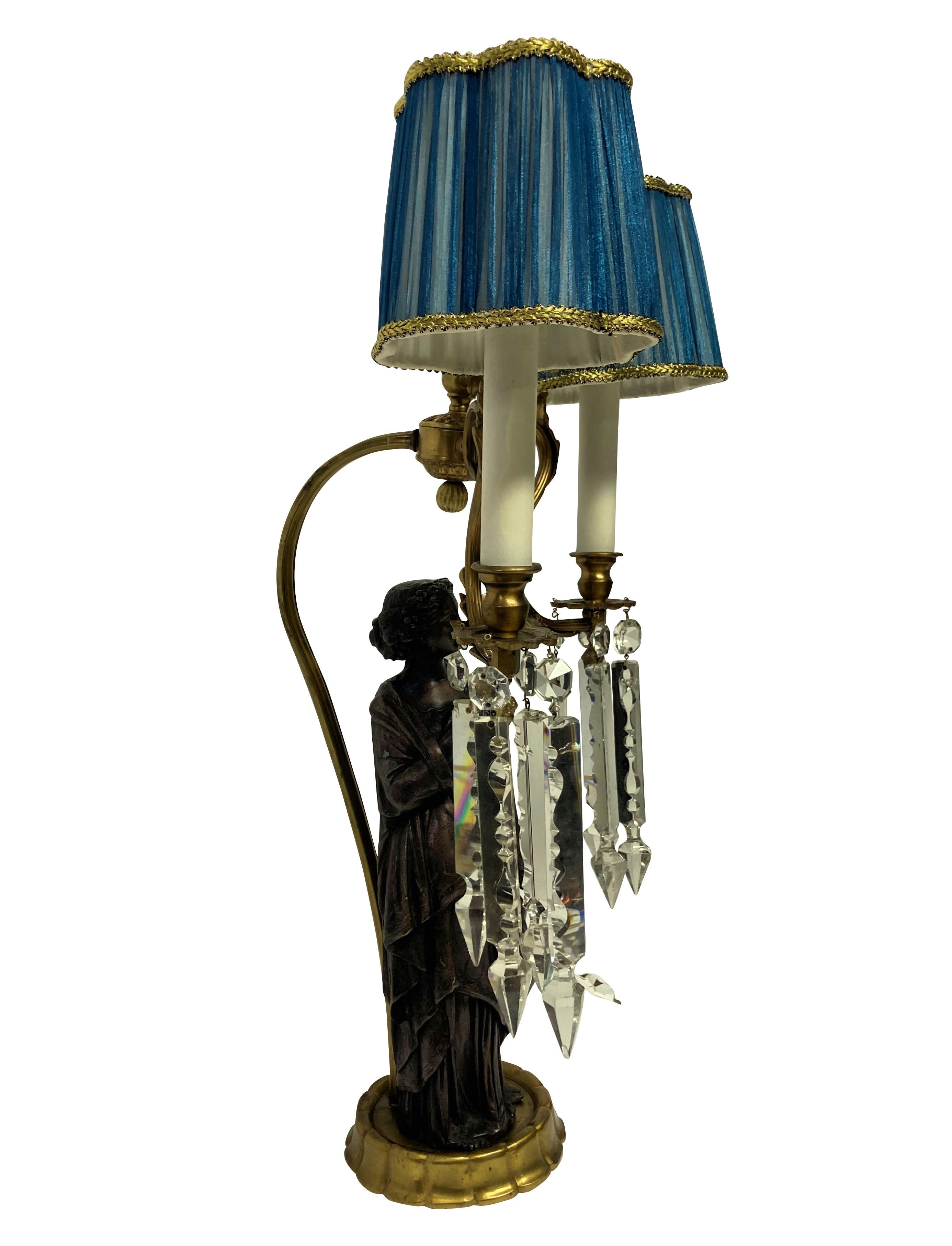 A pair of Italian Classical figural lamps depicting woman in Roman dress, each with cut glass pendant drops and with pale blue silk shades.