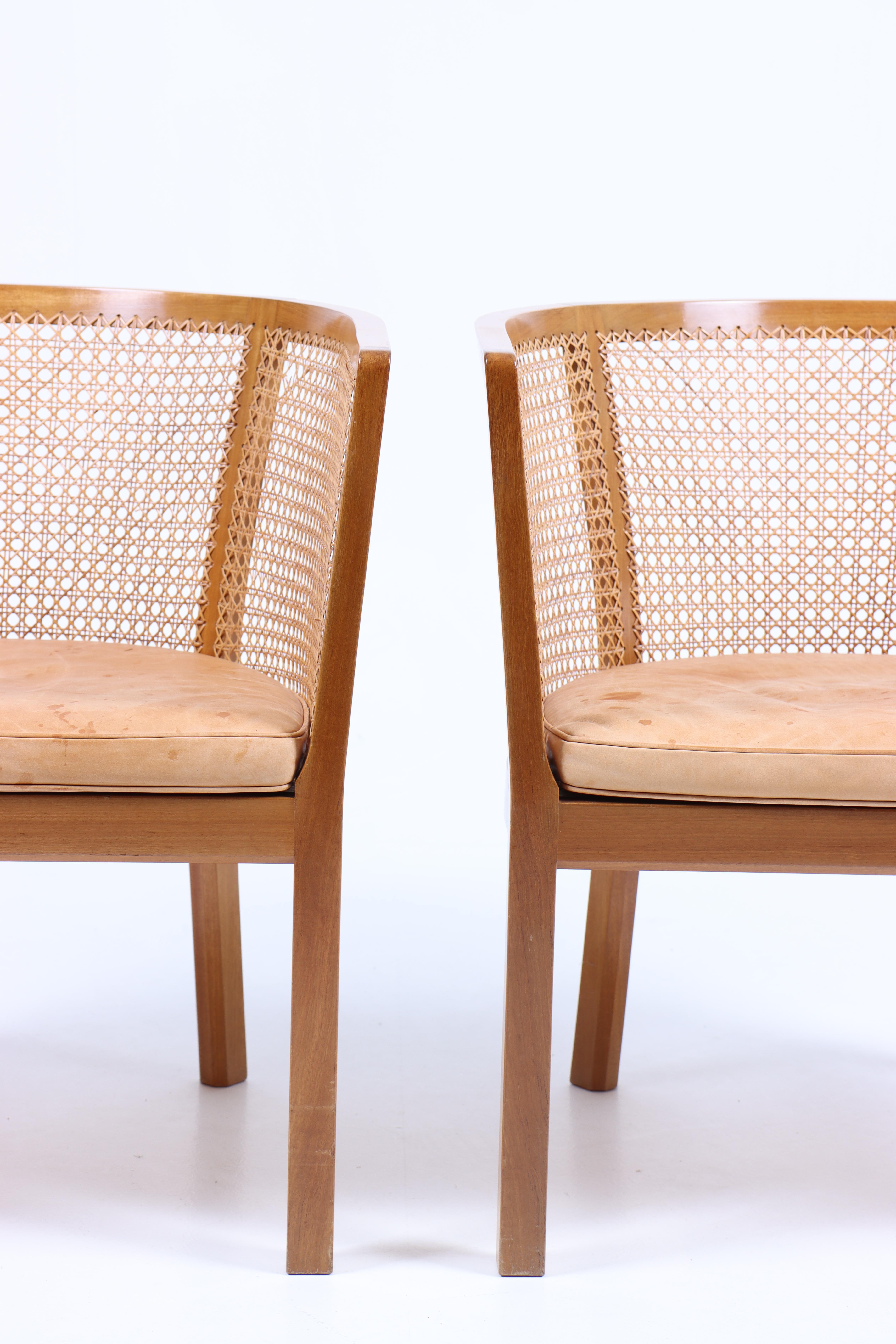 Pair of elegant lounge chairs in solid mahogany and French caning. Seat cushion in patinated leather. Designed by Danish architect Bernt Pedersen.