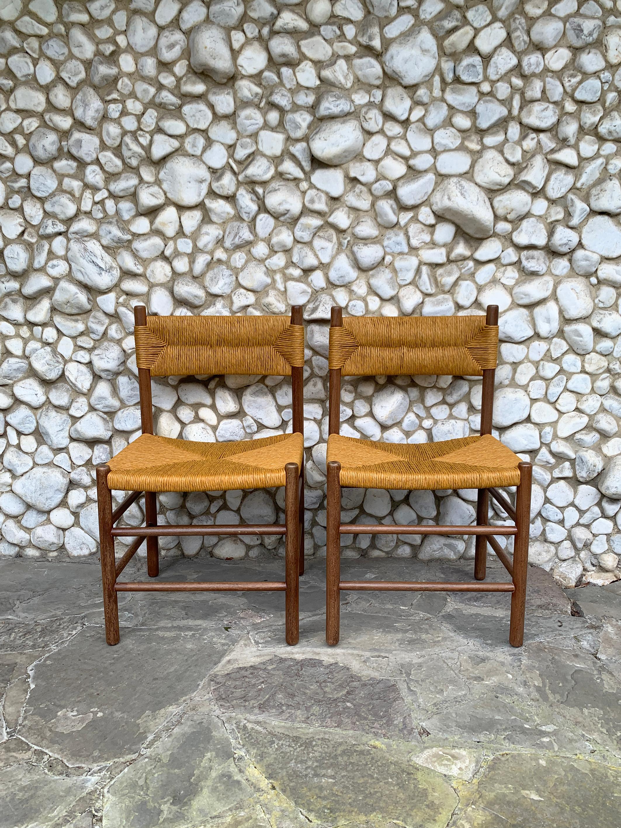 A Pair of French rush/straw dining chairs designed in the style of Charlotte Perriand Dordogne chairs. Produced circa 1960, probably by Robert Sentou, France.

The chairs are made of solid teak-wood. Freshly renewed straw/rush seats and backrests by
