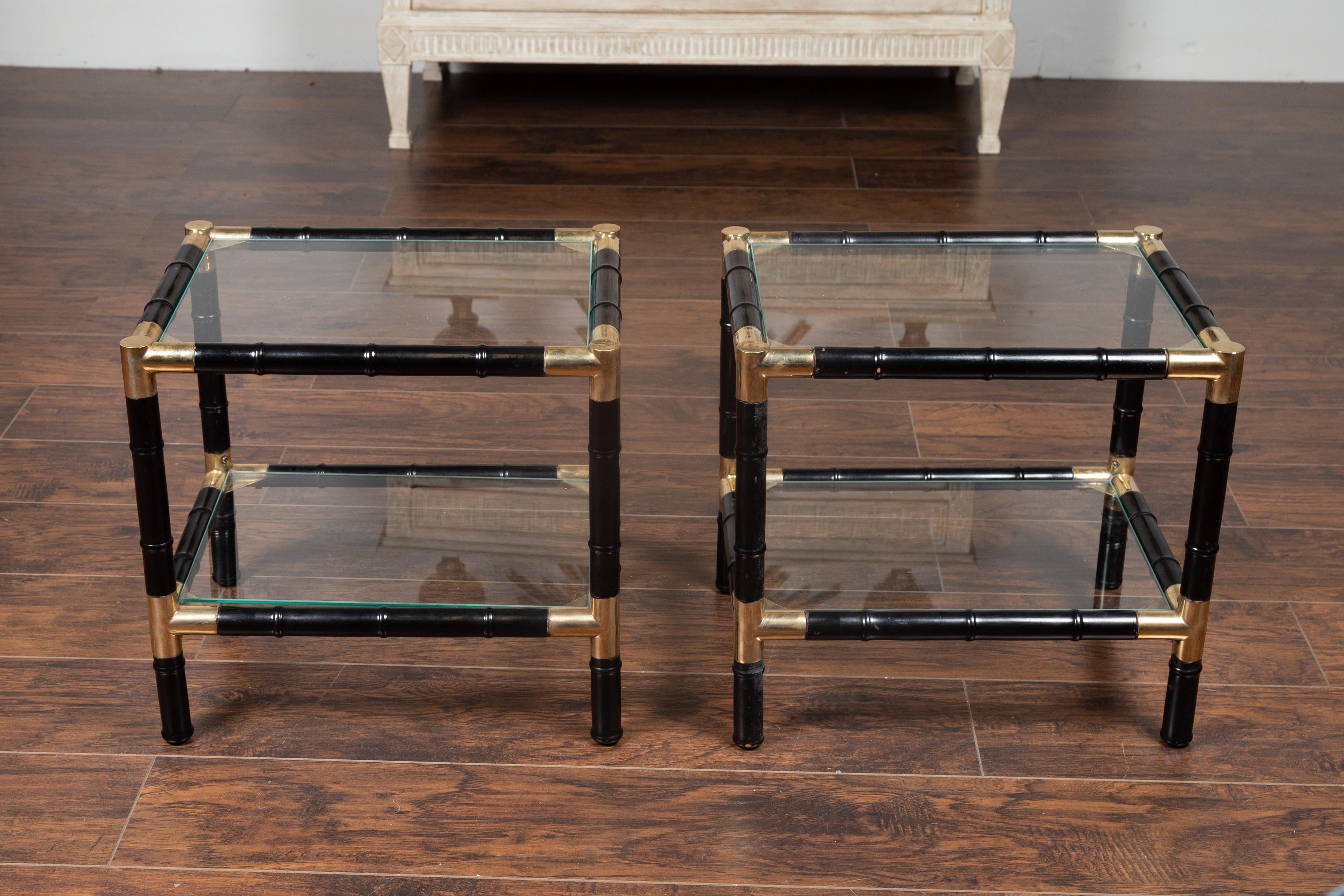 A pair of French vintage ebonized faux bamboo tiered side tables from the mid-20th century, with glass shelves and brass accents. Born in France during the midcentury period, each of this pair of side tables charms us with its contrasting colors and