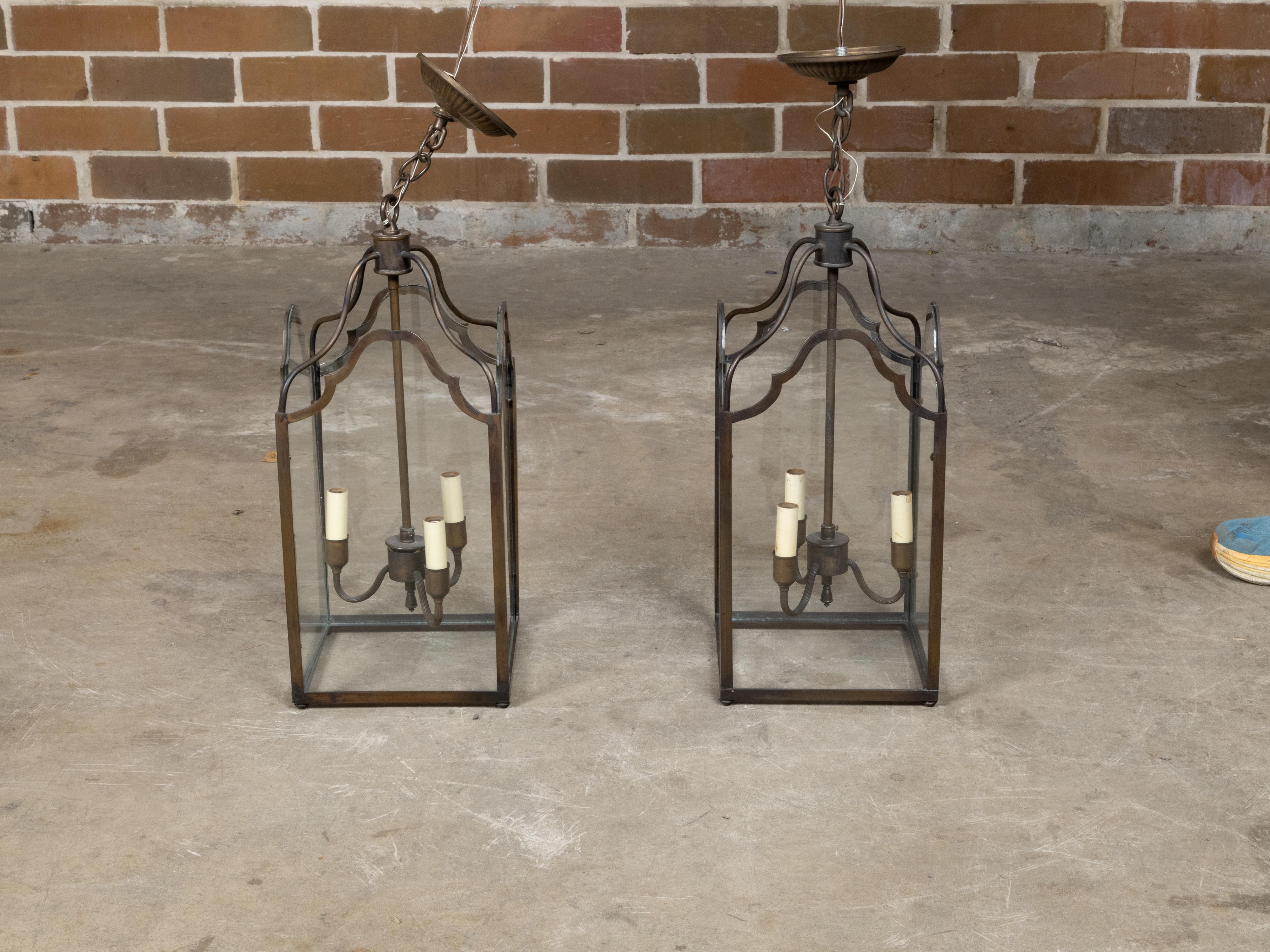 Paire de lanternes en bronze anglaises à trois lumières de la période du milieu du siècle, avec des panneaux en verre. Créée en Angleterre au cours de la période du Midcentury, cette exquise paire de lanternes à trois lumières en bronze séduit par