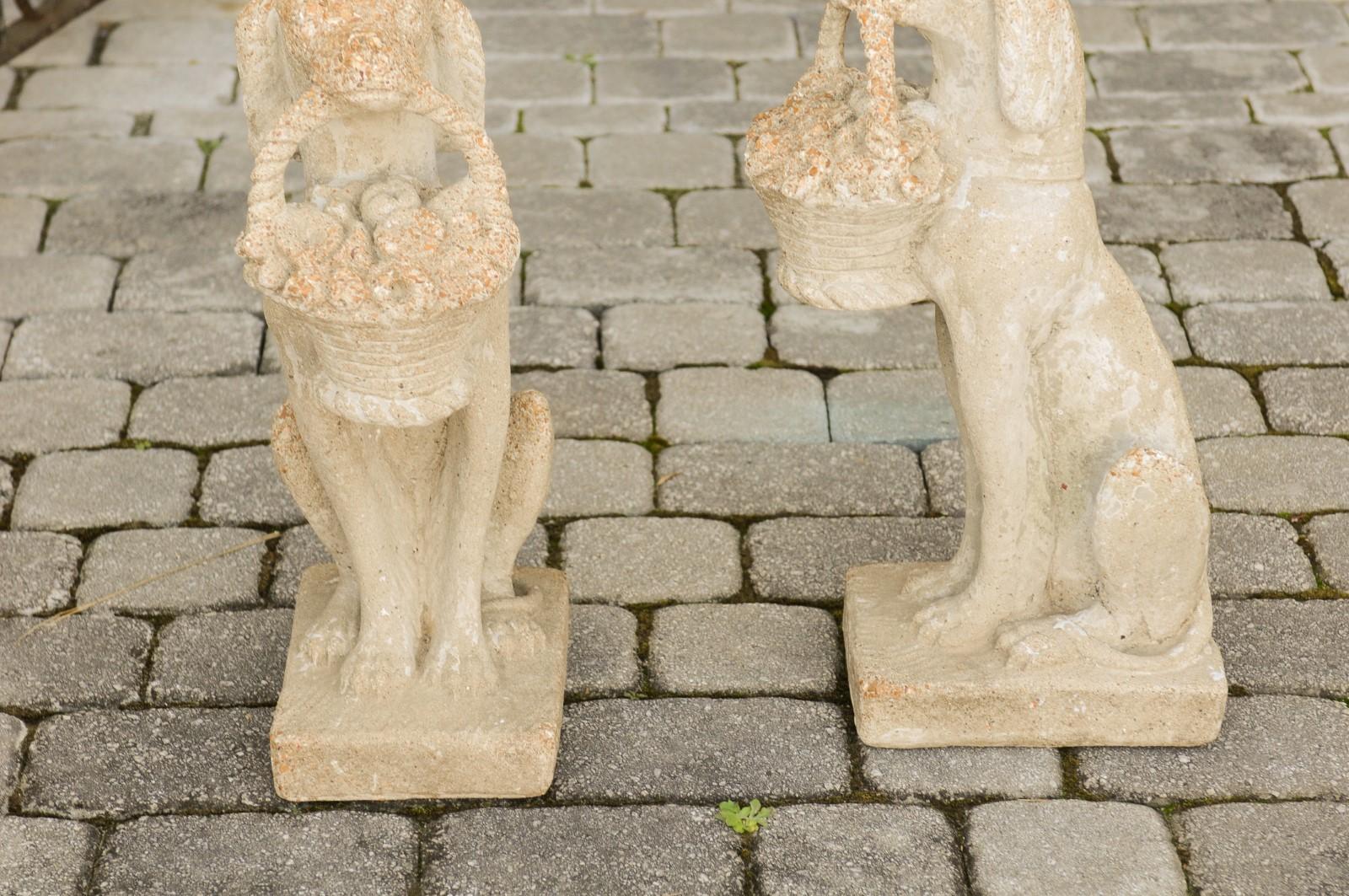 A pair of English vintage cast concrete and rock pebbles dog sculptures from the mid-20th century carrying baskets of flowers in their mouth. Born in England during the midcentury period, each of this pair of English sculptures features a graceful