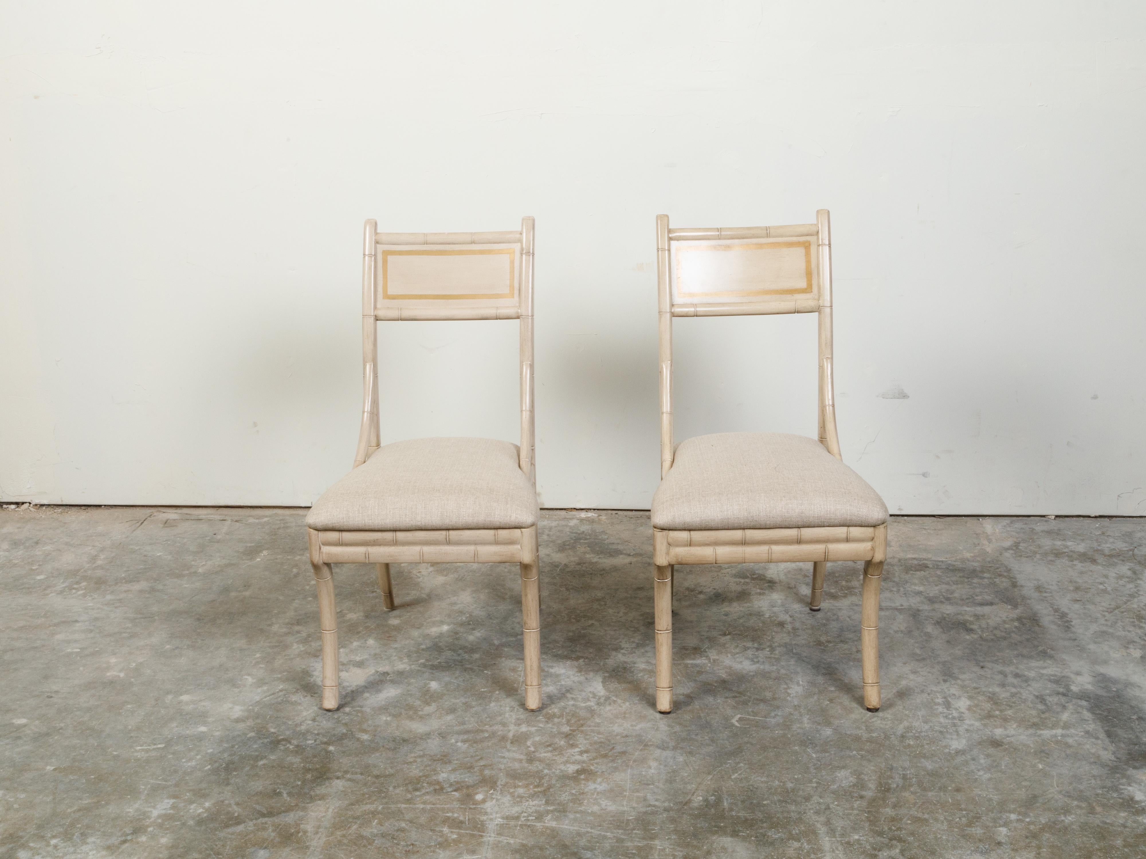 A pair of faux bamboo side chairs from the mid 20th century with saber legs and new linen upholstery. Created during the midcentury period, each of this pair of side chairs features a simple back with rectangular support, flowing seamlessly into the