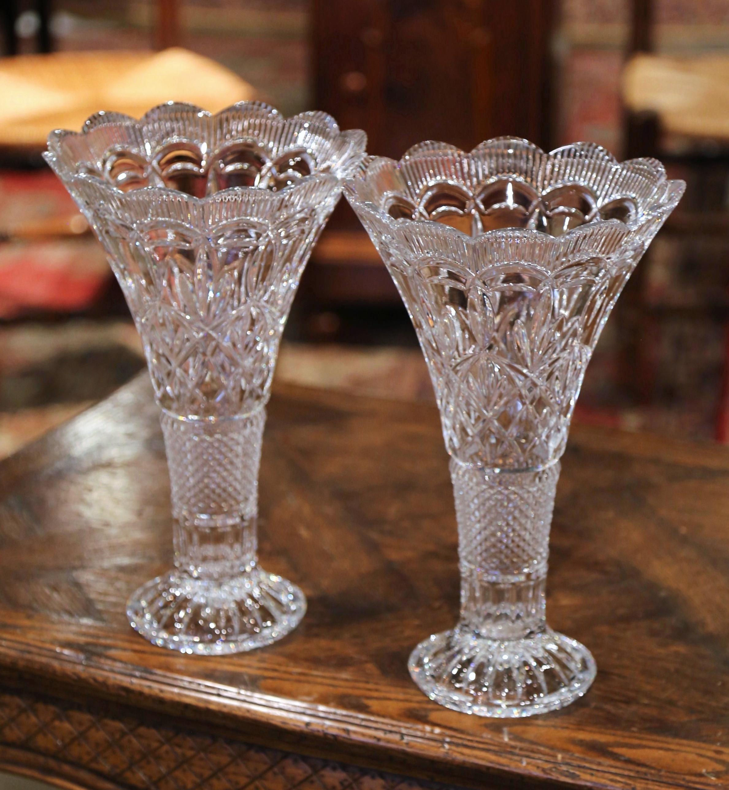 Decorate a console or buffet with this elegant pair of crystal trumpet vases. Crafted in France, circa 1960 and round in shape, the large luxurious cut glass vessels are decorated throughout with geometric and leaf decor; the vessels are further