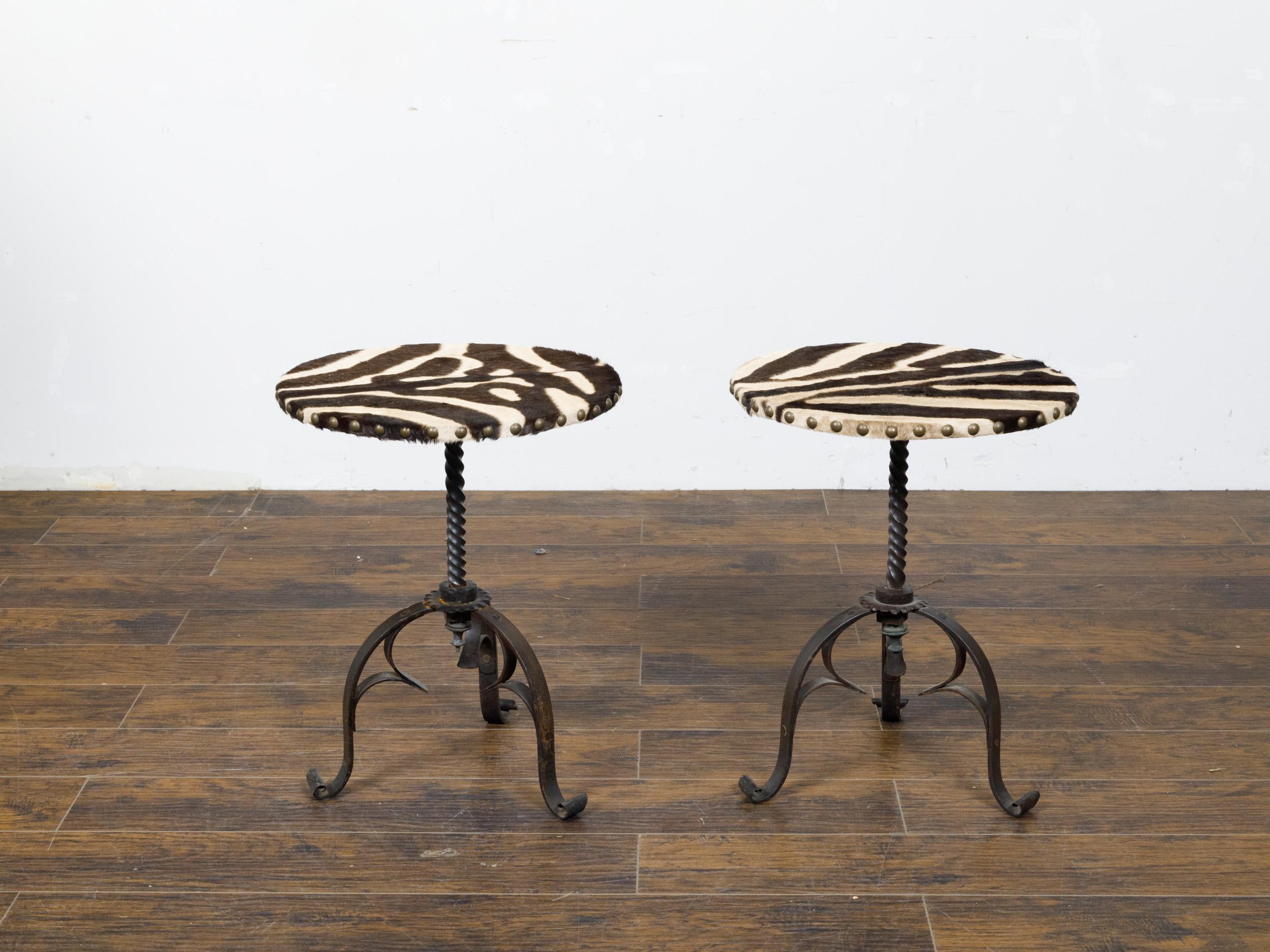 A pair of French iron guéridon side tables from the mid 20th century with round zebra hide tops, twisted bases on three scrolling legs. This captivating pair of mid-20th century French guéridon side tables exudes a unique blend of rustic charm and