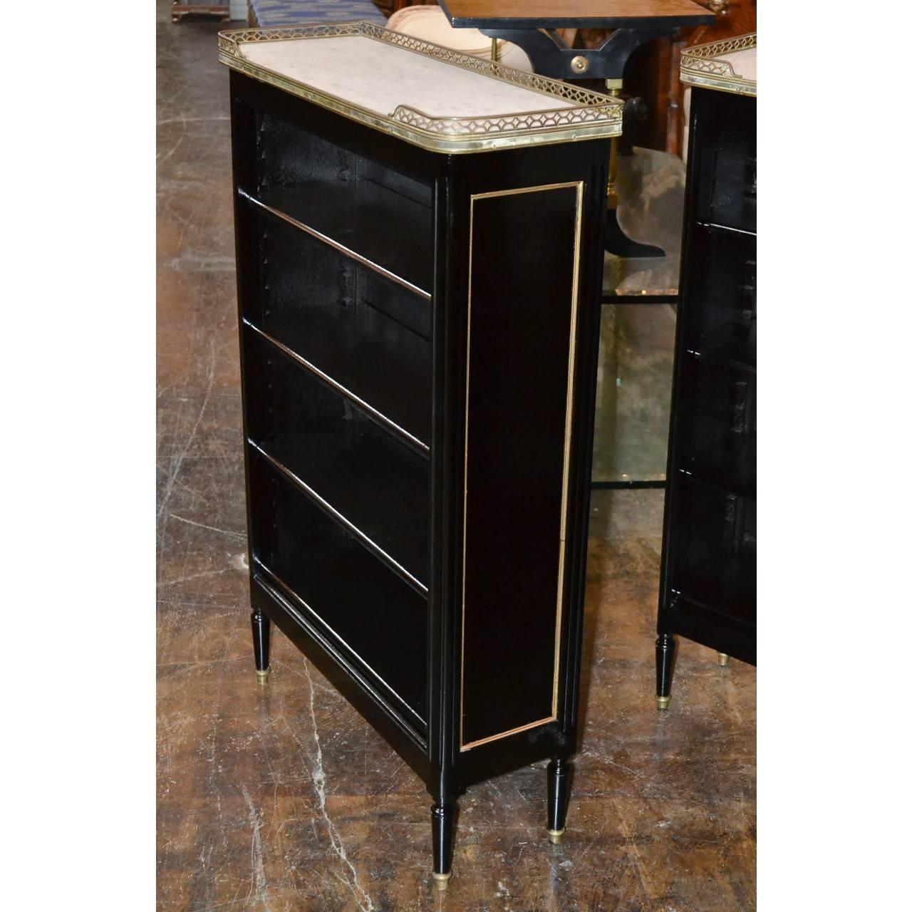 Fabulous pair of midcentury French black lacquered bookcases with gray-veined white marble tops having filigree brass borders. Accented overall with brass trim and raised on turned and tapered legs with brass capped feet,

circa 1940.

Great