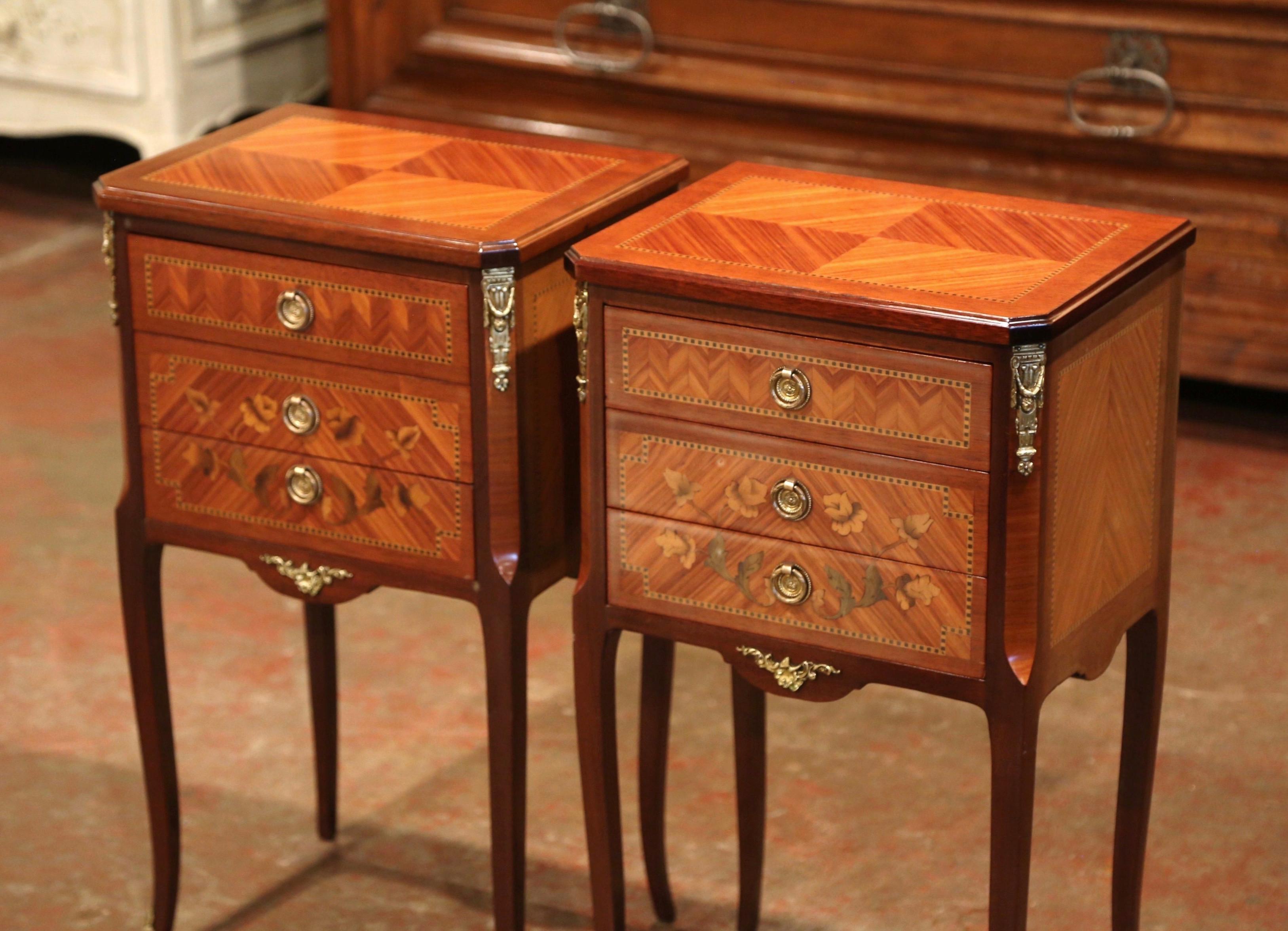 These elegant vintage bedside tables were created in France, circa 1950; each chest stands on cabriole legs with front sabots over a scalloped apron dressed with a bronze mount. The cabinet features three drawers decorated with floral marquetry