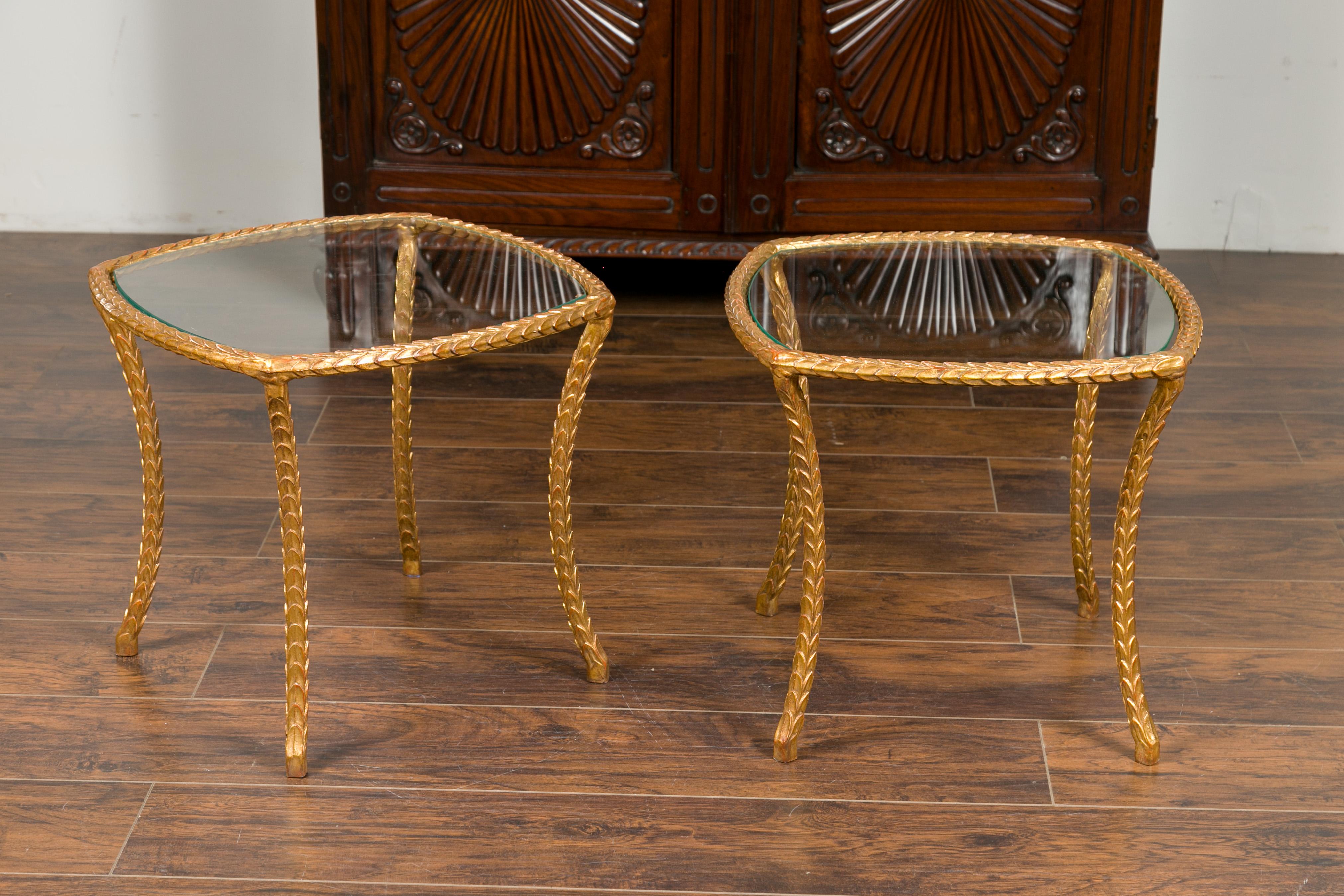 A pair of vintage French gilt bronze Maison Baguès style side tables from the mid-20th century, with stylized foliage motifs and glass tops. Crafted in France during the midcentury period, each of this pair of Maison Baguès style tables features a