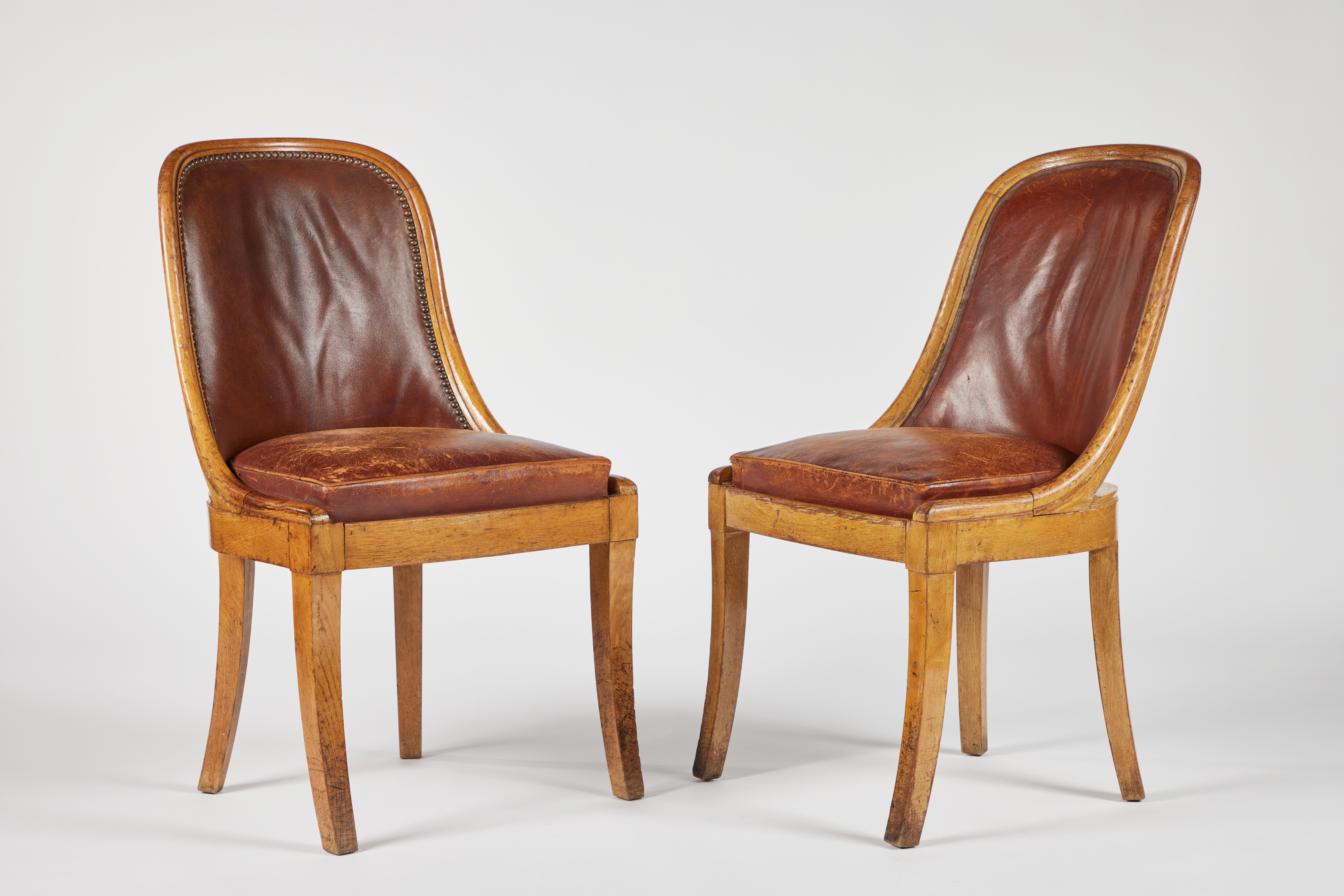 A pair of French sabre-leg oak side chairs with original leather upholstery, original sticker marked INVENTAIRE 1959.