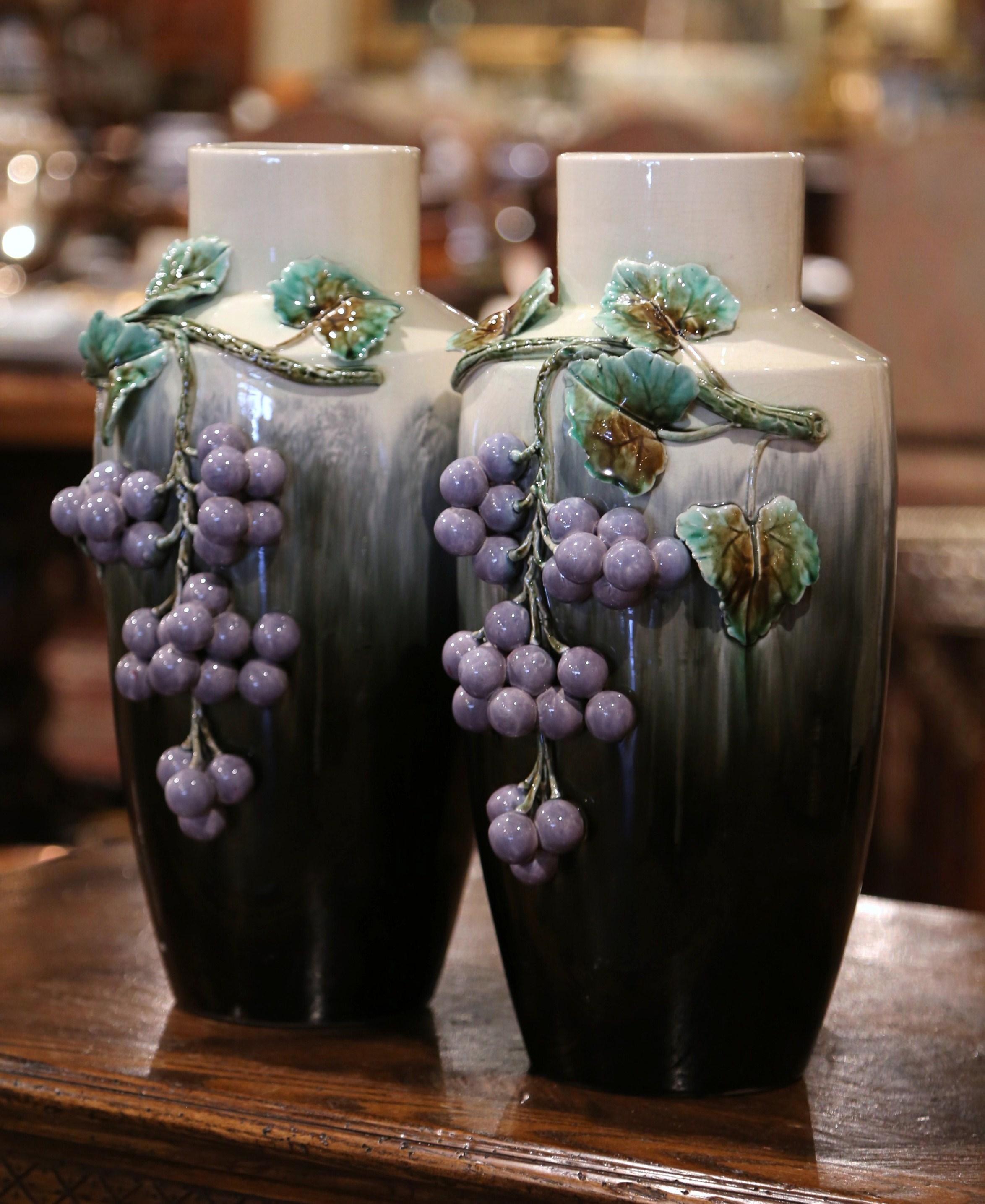 Crafted in France circa 1950 and round in shape, each tall vase is decorated with grape and leaf motifs in the green and purple palette. Both porcelain vessels are in excellent condition and stamped on the bottom for further authentication. Decorate