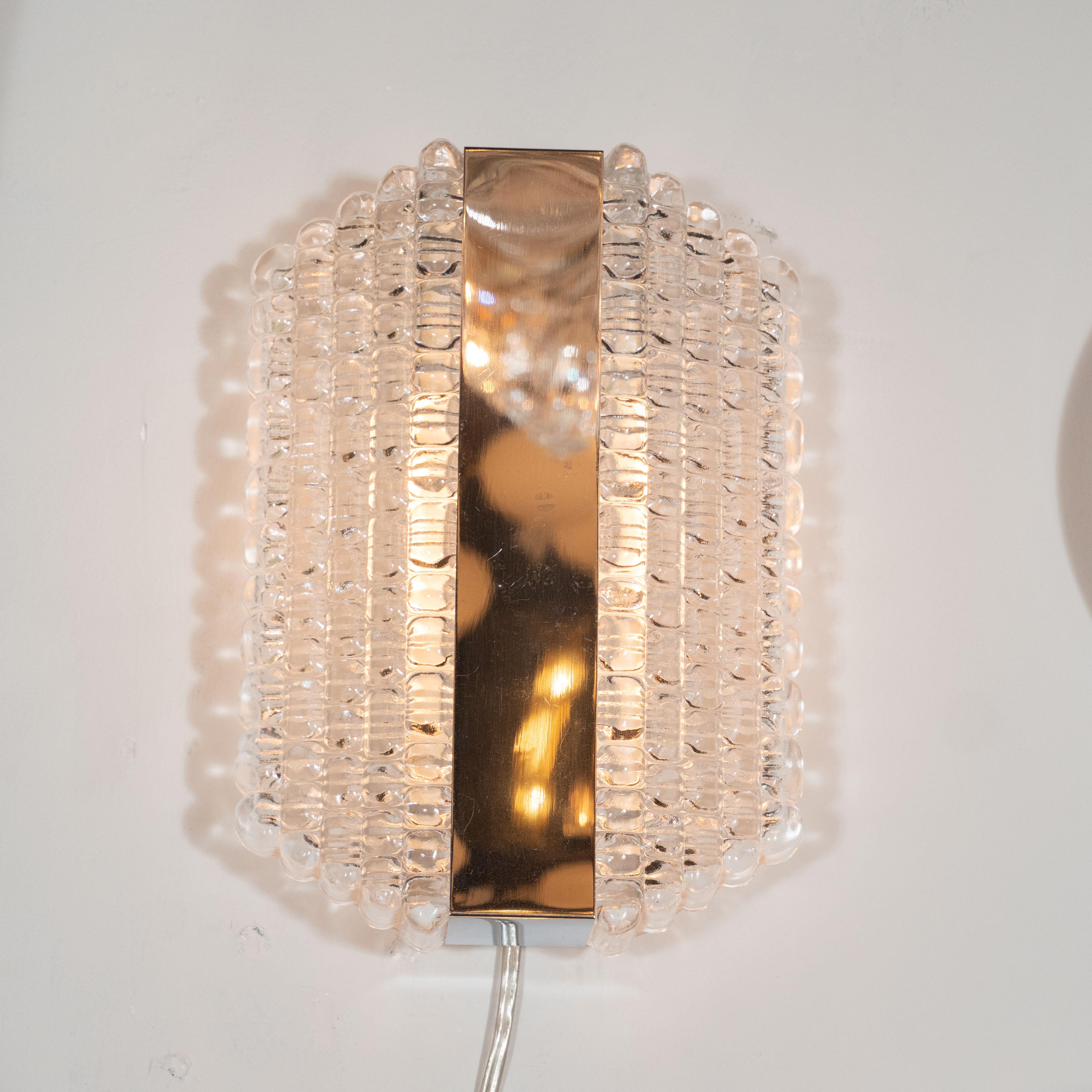 This refined pair of Mid-Century Modern sconces were realized by the esteemed glass studio Kaiser Leuchten in Germany, circa 1960. They feature five rows of touching textured glass on each side that diminish in height and depth to each edge,