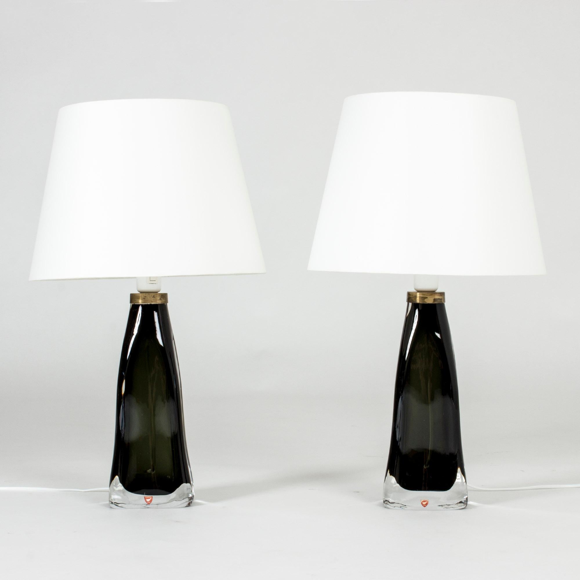 Pair of inky dark green, semi-translucent glass table lamps by Carl Fagerlund for Orrefors. Heavy glass bases with a somewhat undulating shape and brass detail at the top. Very elegant and beautiful in a window.
