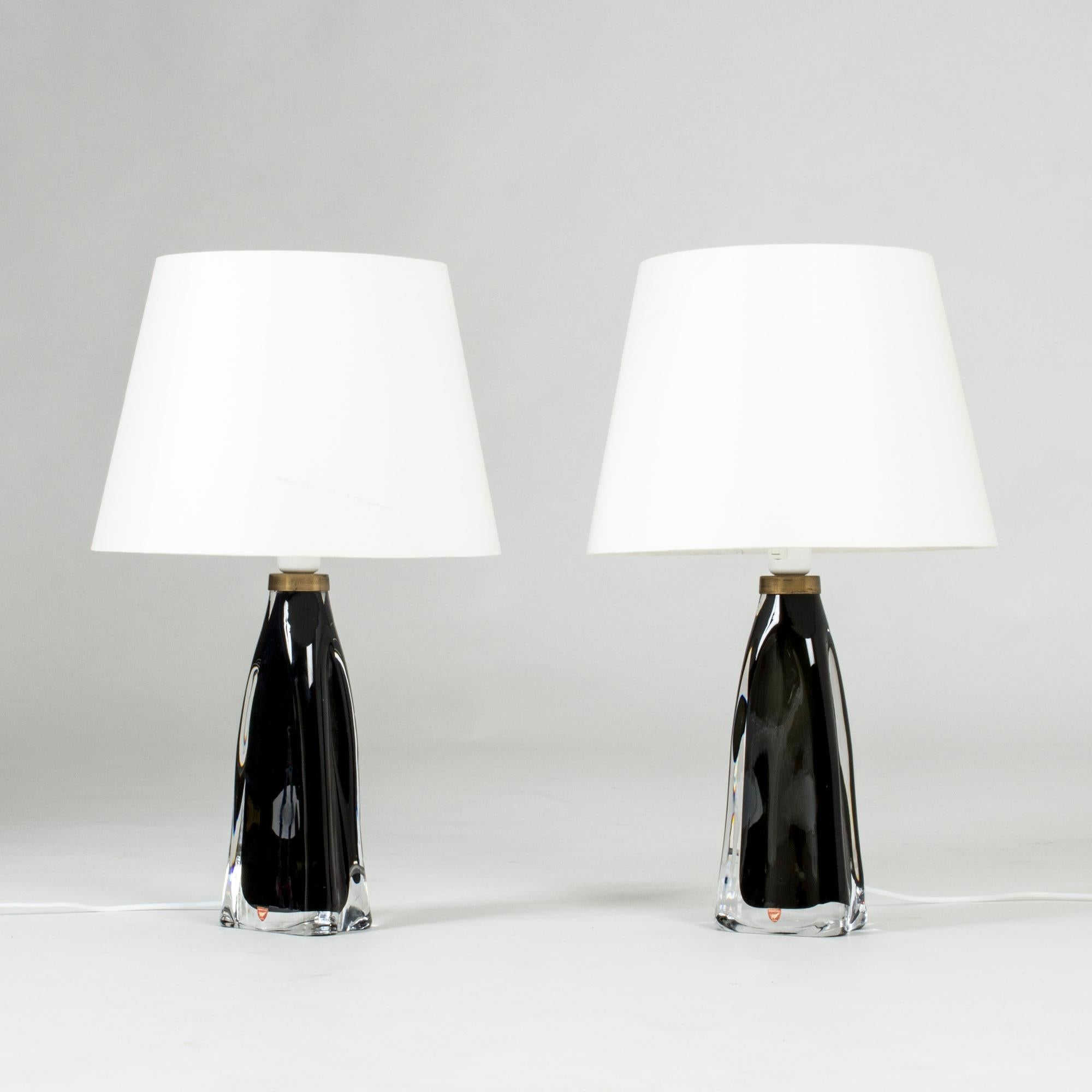 Pair of black, barely translucent glass table lamps by Carl Fagerlund for Orrefors. Heavy glass bases with a somewhat undulating shape and brass detail at the top. Very elegant with movement in the design.