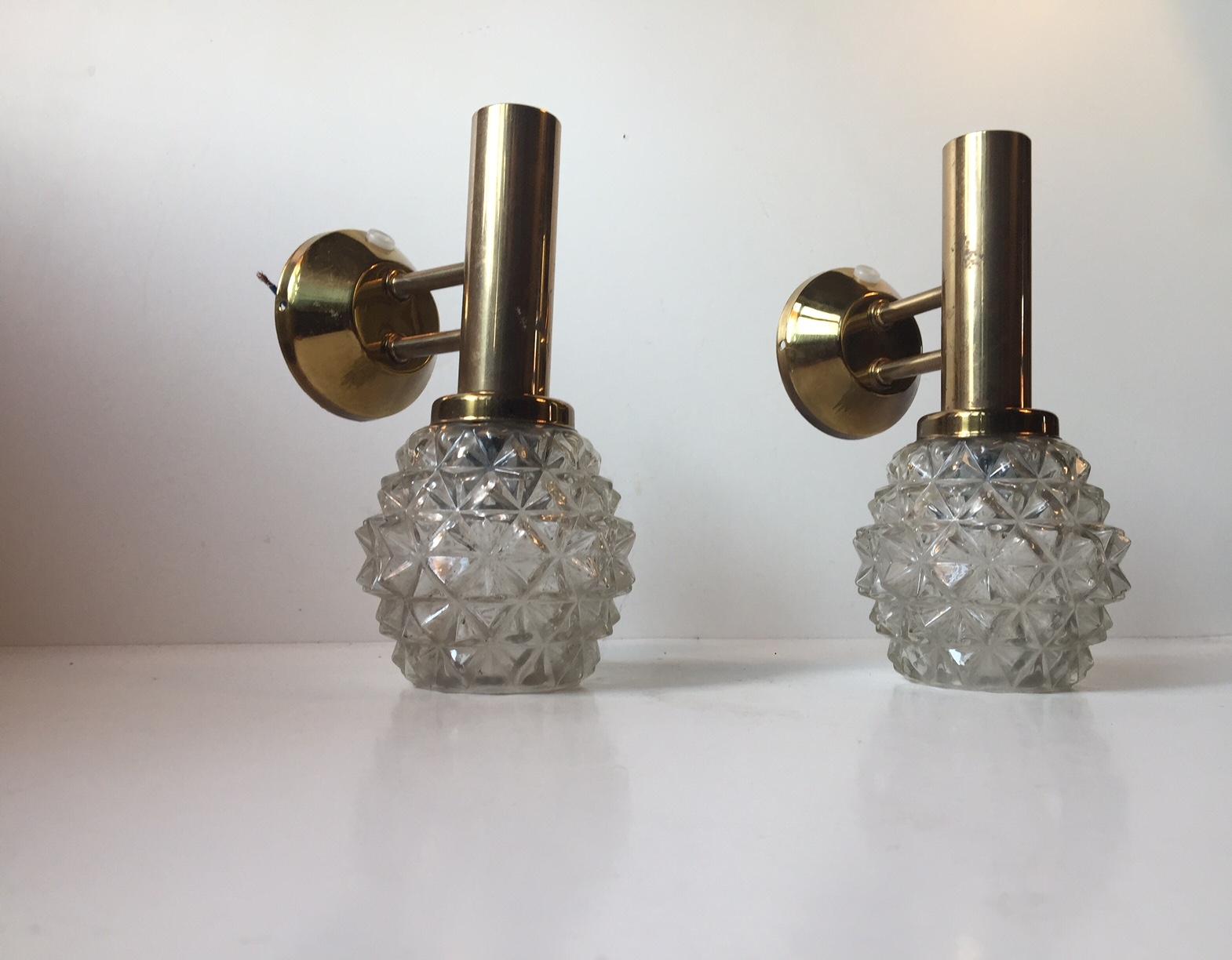 A pair of granat-shaped sconces in pressed clear glass and brass. Anonymously manufactured in Scandinavia during the 1960s in a style reminiscent of Carl Fagerlund, Hans Agne Jakobsson and CT. Kalmar.