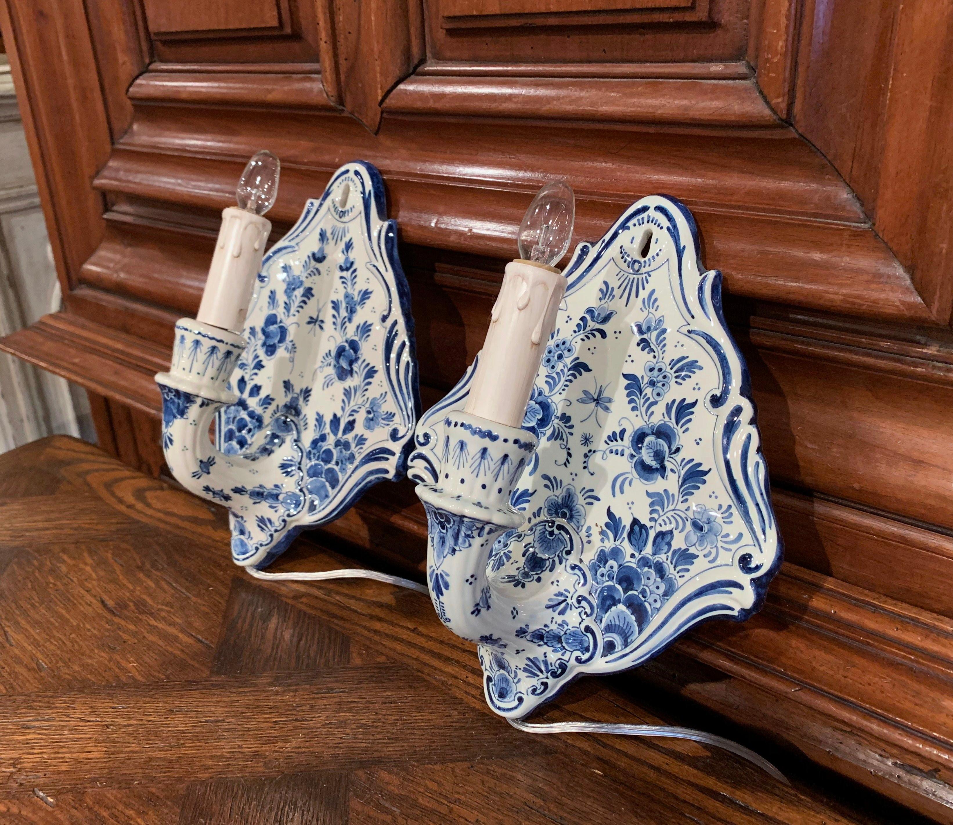 Decorate a powder room with this elegant pair of ceramic sconces, crafted in Holland circa 1950, each single light has new wiring embellished with a decorative candle sleeve; the fixture is hand painted with blue and white floral and leaf decor in