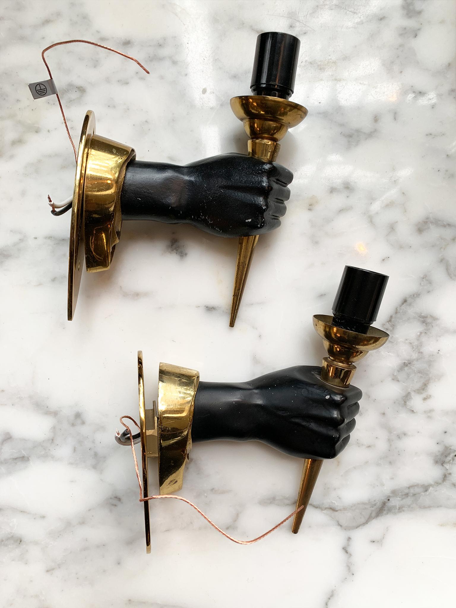 A pair of neoclassical handform sconces, mid-20th century. Designed in the style of André Arbus. They are comprised of brass backplates, brass candleholders, and black-painted metal hands. Each sconce is newly rewired.

Dimensions:
3 1/16 in.