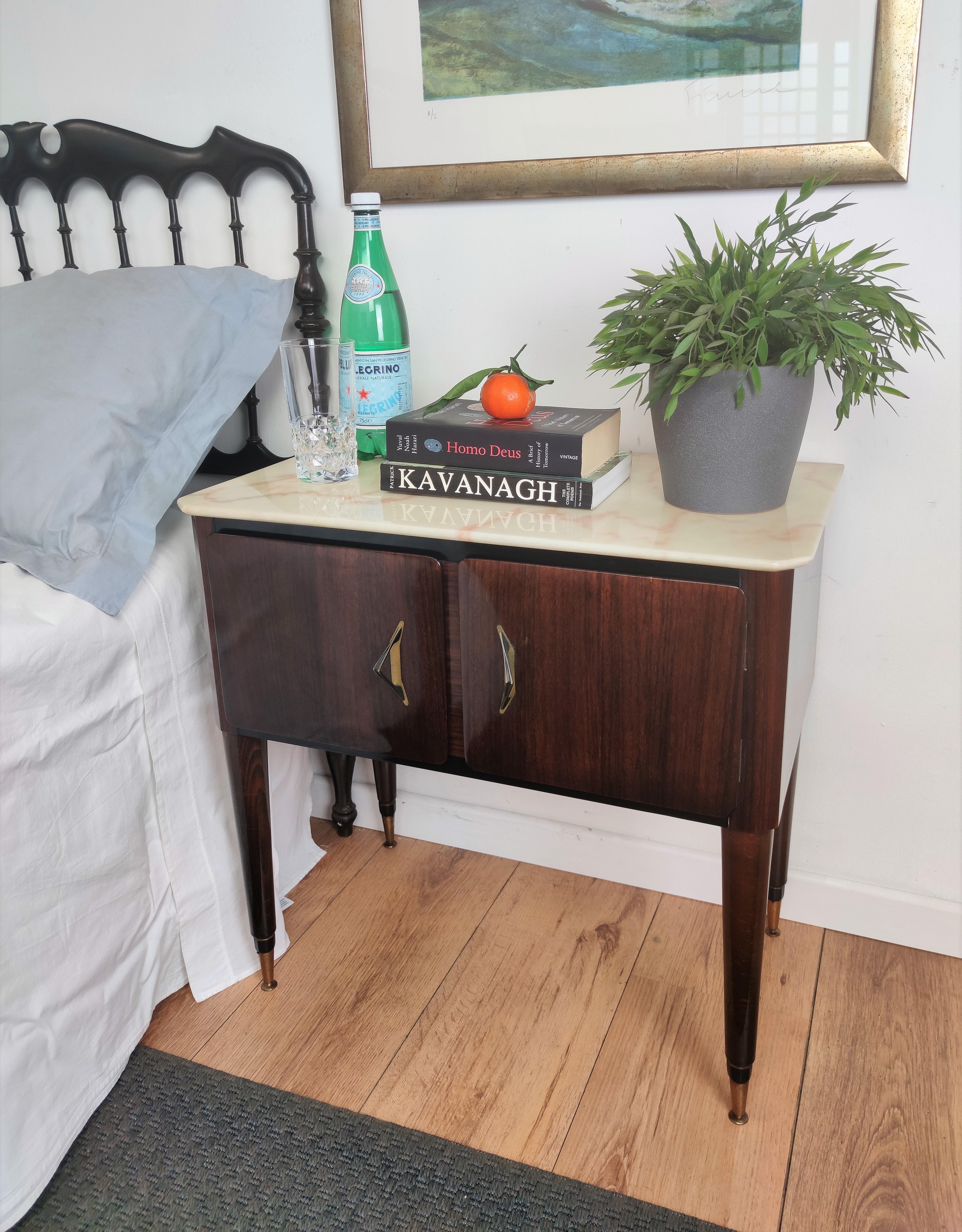 Very elegant and refined Italian 1950s Mid-Century Modern, neoclassical, in typical Art Deco design, pair of bedside tables with wood double front door, white marble top and brass details such as the 2 handles and the 4 foot ends. 

Those pieces,