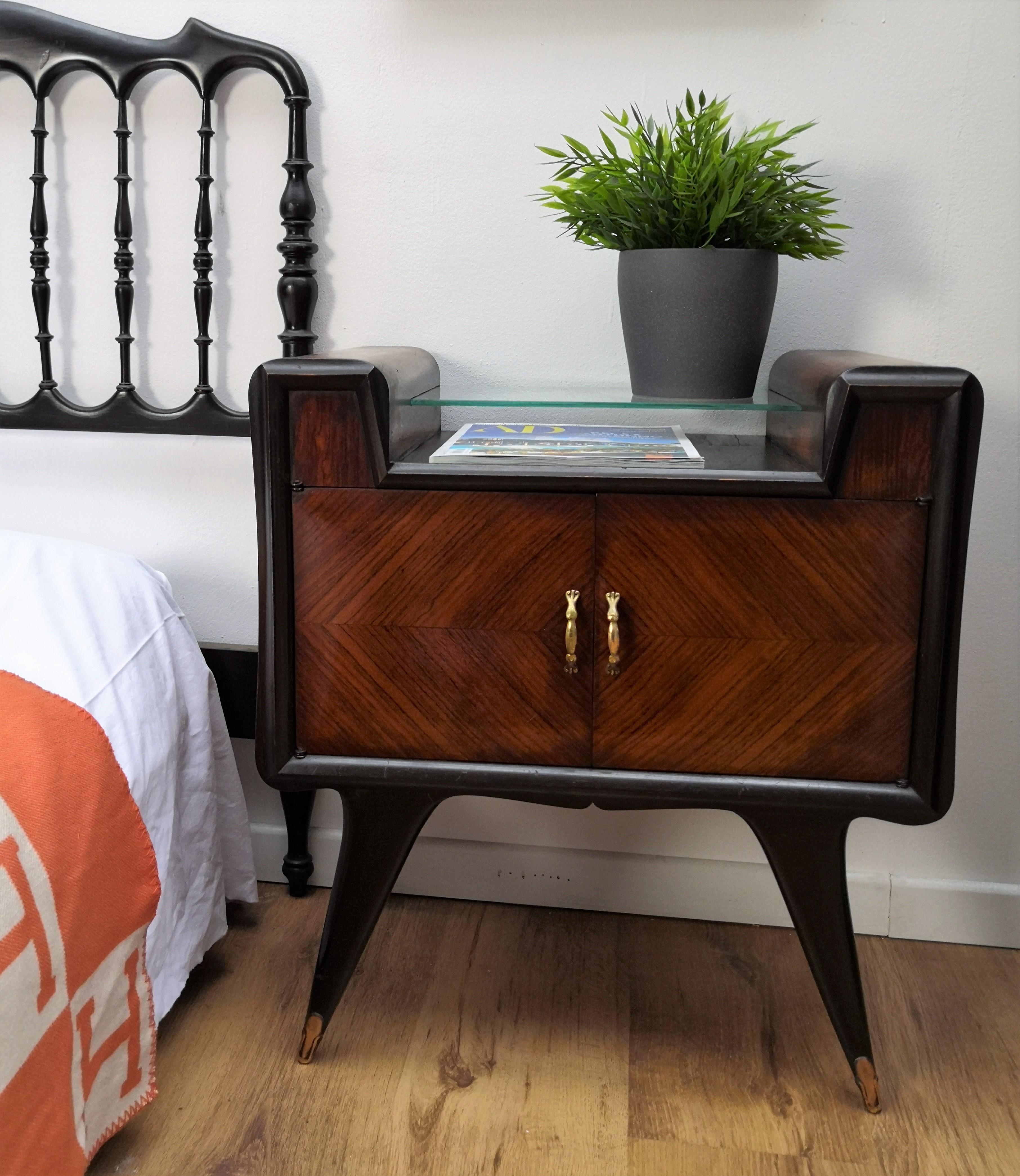 Very elegant and refined Italian 1950s pair of bedside tables, nightstands with rosewood double front door, central glass top and brass details such as the 2 handles and the 4 foot ends. Those charming pieces are in the typical Art Deco design, in