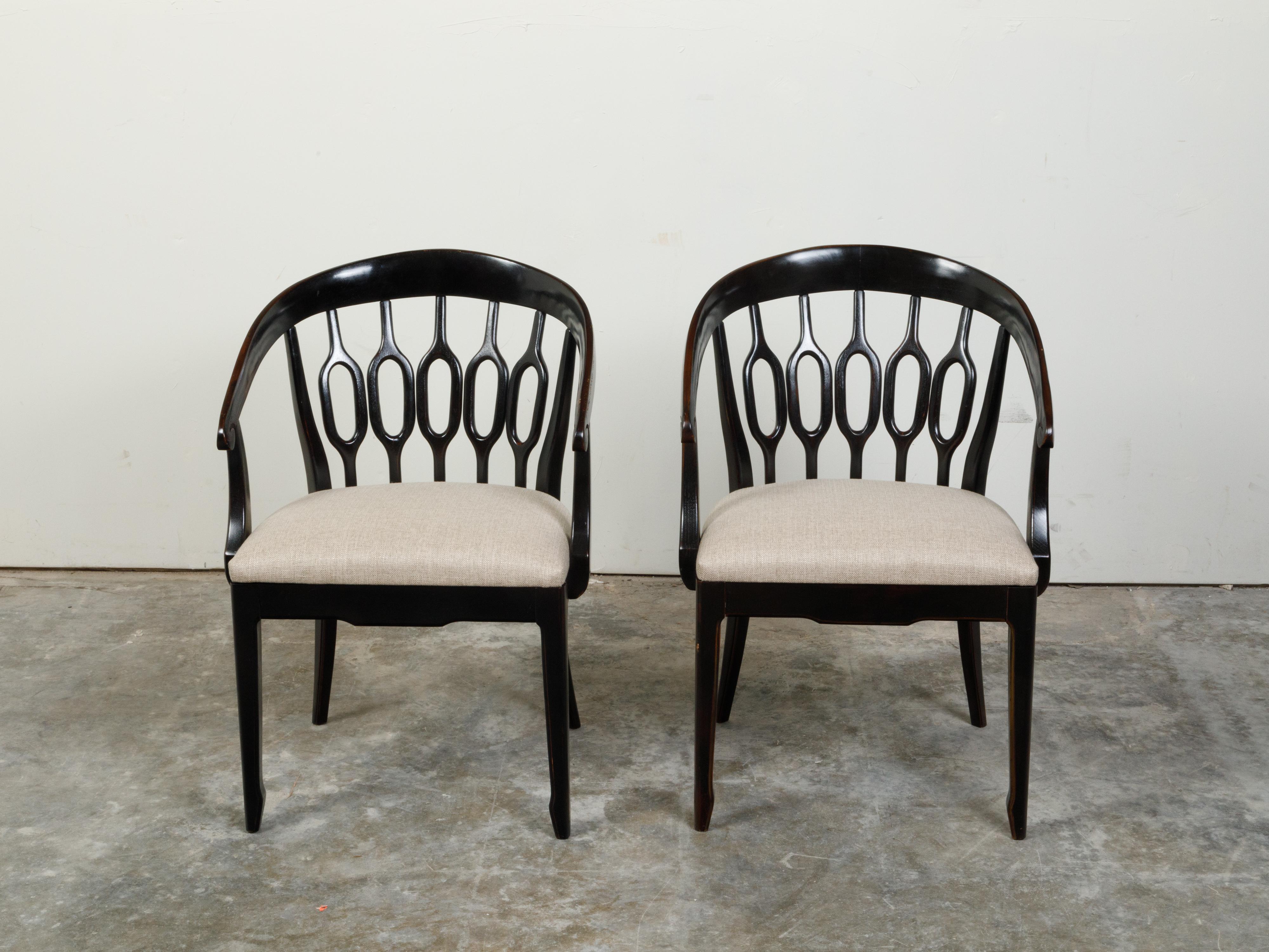 A pair of Italian black carved wooden horseshoe armchairs from the mid 20th century, with pierced splats and new upholstery. Created in Italy during the midcentury period, each of this pair of armchairs features a horseshoe back adorned with pierced