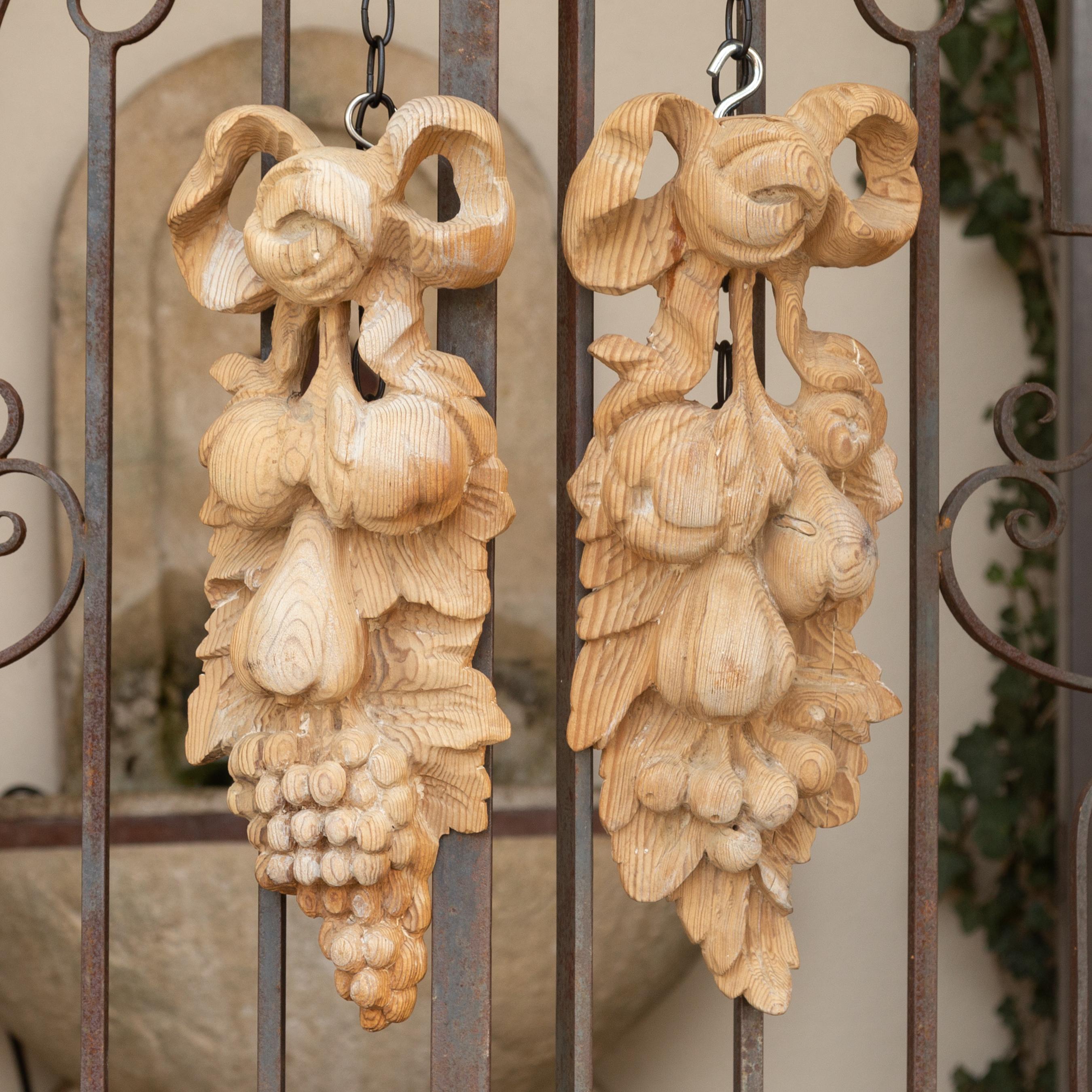 A pair of vintage Italian bleached wood wall carvings from the mid-20th century, depicting ribbon-tied fruits. Born in Italy during the midcentury period, each of this pair of wall carvings depicts a ribbon-tied arrangement of high-relief pears and