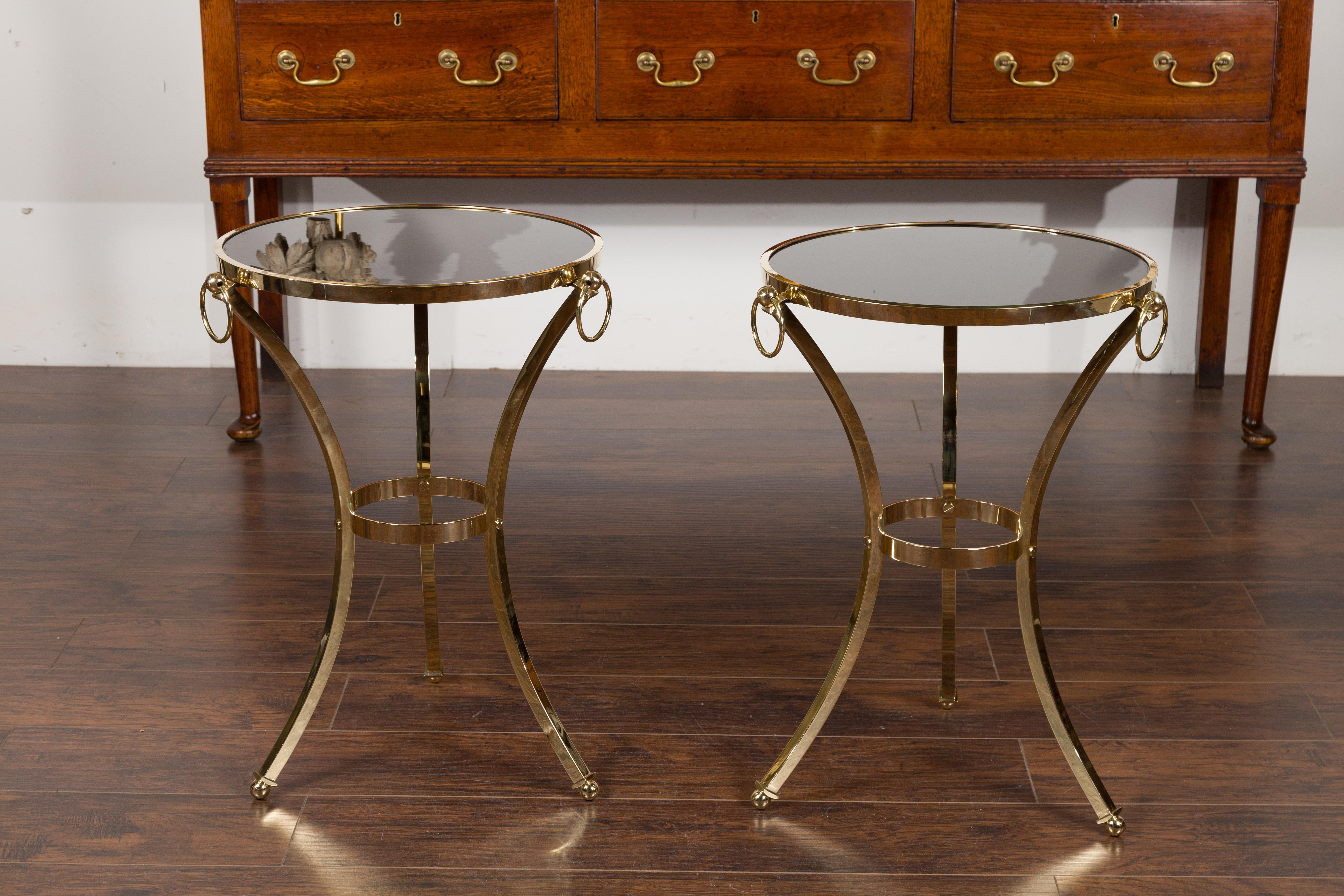 A pair of vintage Italian brass tables from the mid-20th century, with black mirrored tops and ring motifs. Created in Italy during the midcentury period, each of this pair of side tables features a circular round top showcasing a black mirror. The