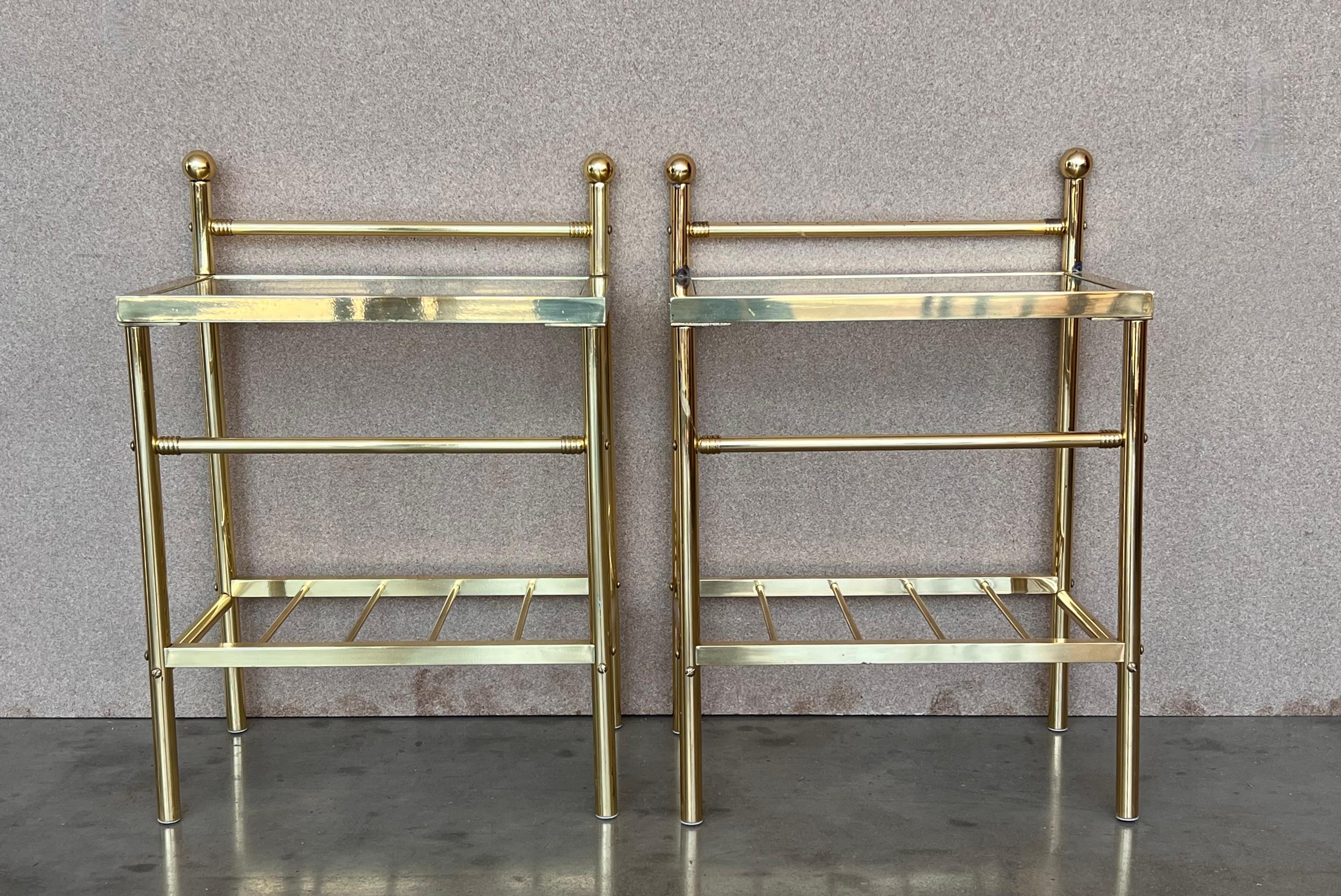 Pair of midcentury Italian two tier brass and glass nightstands with crest.
Simple tables with a low grid shelve and glass top. 

Height to the glass top :20.70in.