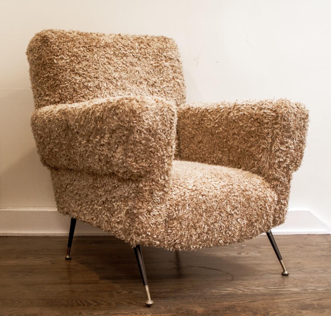 A pair of midcentury Italian sculptural armchairs in a biscuit color faux lambswool, circa 1950. Reminiscent of giant teddy bears, the oversize chairs sit on splayed metal legs with brass sabots. 

Provenance: Obsolete.