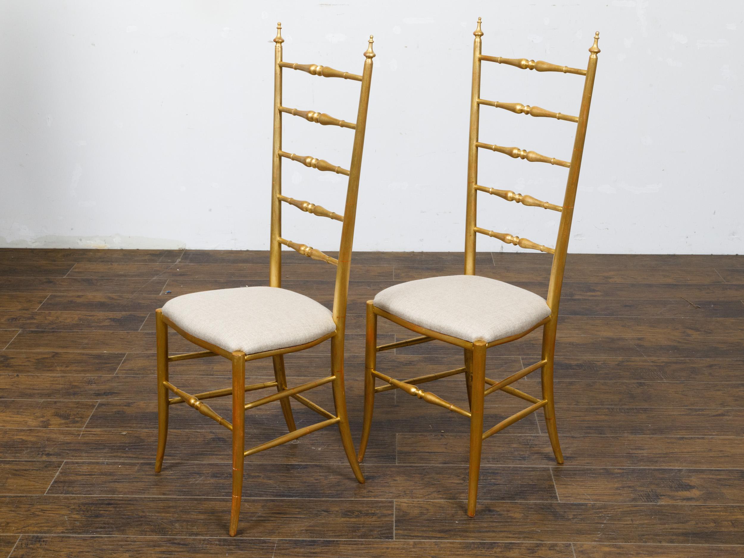 A pair of Italian Midcentury gilt wood high back side chairs with spindle motifs and new custom upholstery. This captivating pair of Italian Midcentury gilt wood high back side chairs embodies the elegance and charm of post-war Italian design. With