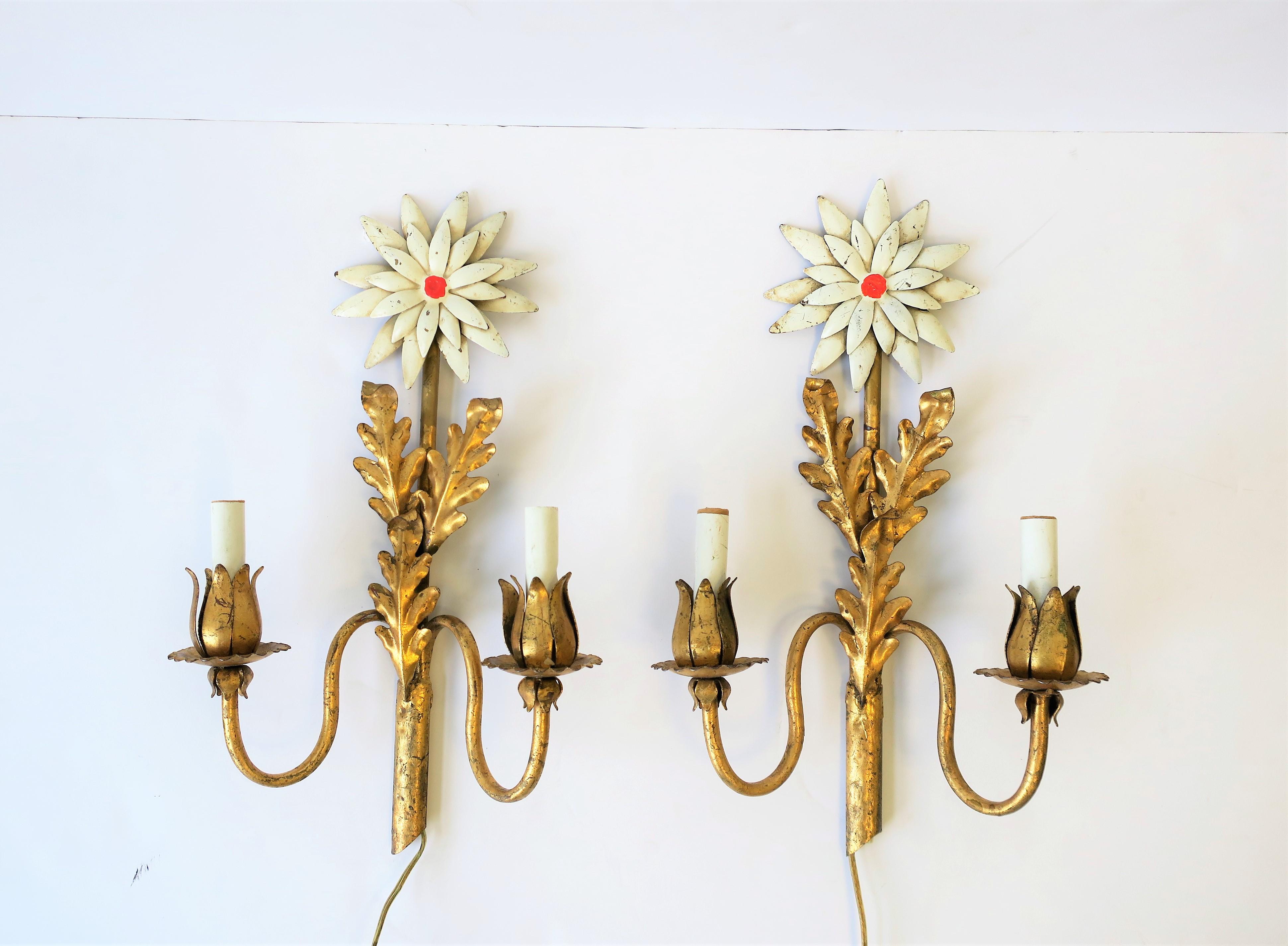 A beautiful and rare pair of midcentury Italian gold gilt tole metal wall lights or wall sconces. Each have a white enamel flower with red center, gold gilt tole leaves, and two lights each with gold gilt flower petals. Pair are marked 'Made in