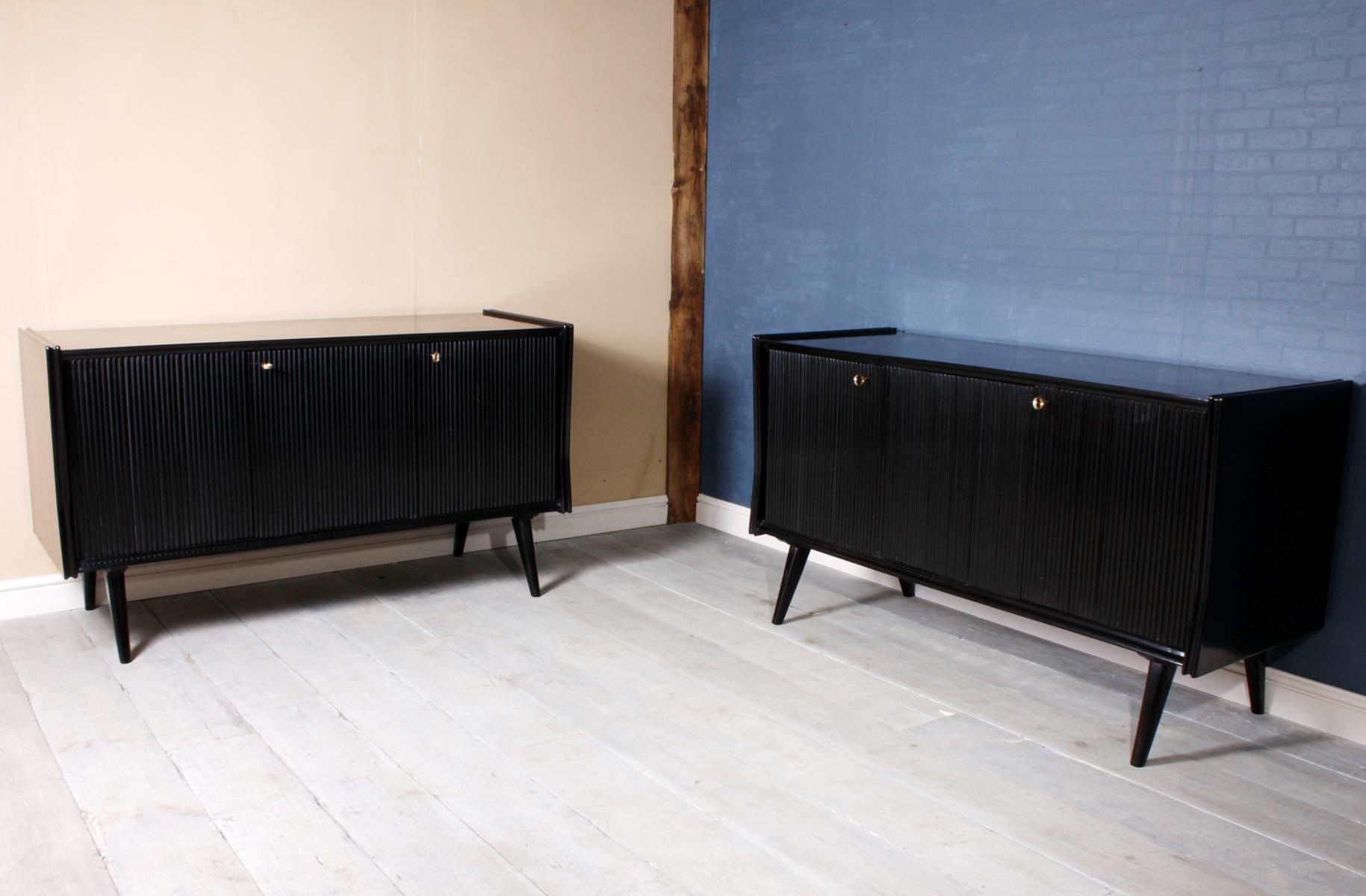 Pair of midcentury Italian piano lacquer sideboards
These three reeded door sideboard are opposite pair one has fitted drawers with glass fronts the other has a dry bar They stand on splayed out legs and have inset brass locks, hinges and keys the