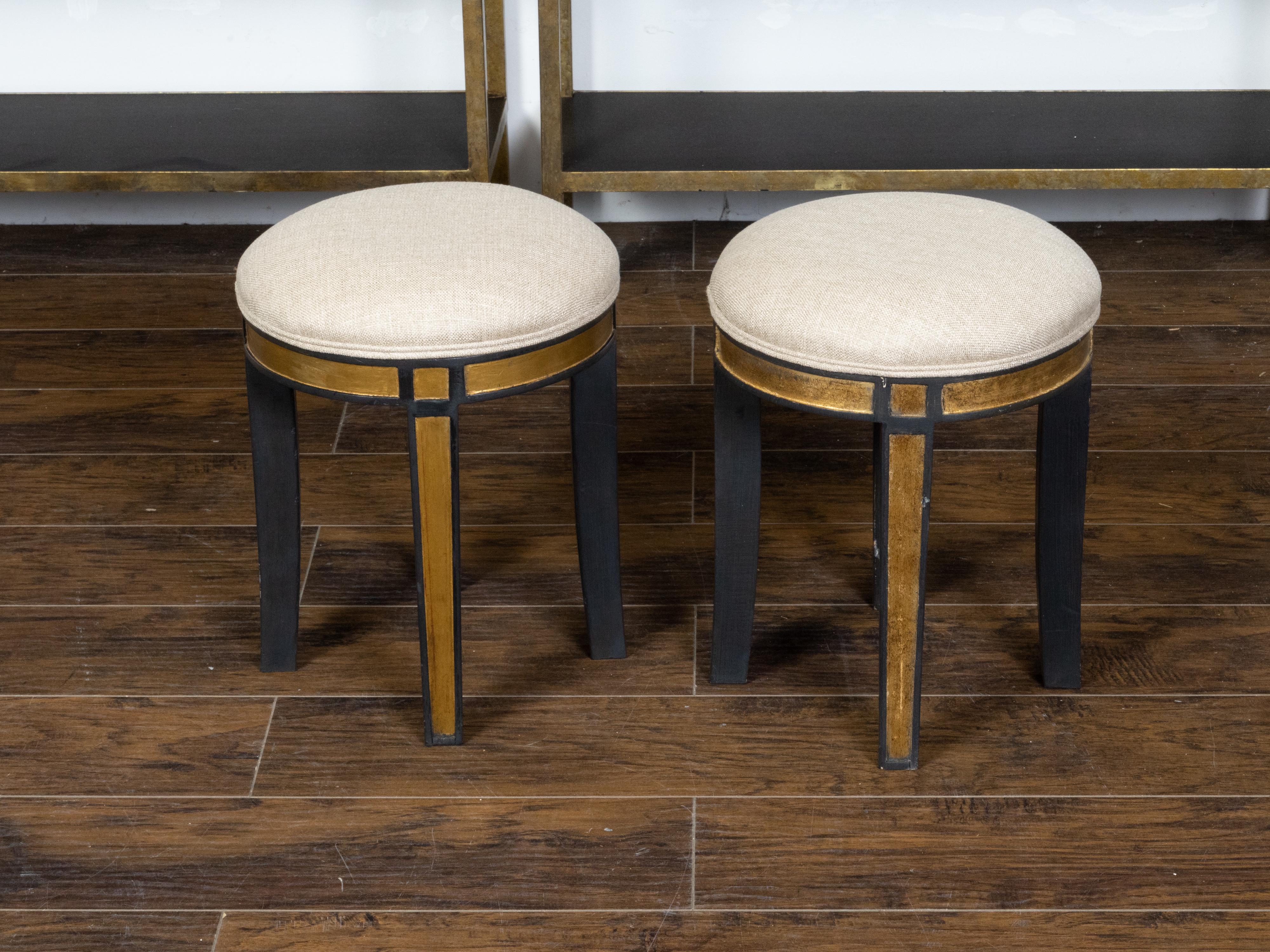 A pair of vintage Italian stools from the mid 20th century, with round upholstered seats, black paint and gilt accents. Created in Italy during the Midcentury period, each of this pair of stools features a circular top newly recovered with a double