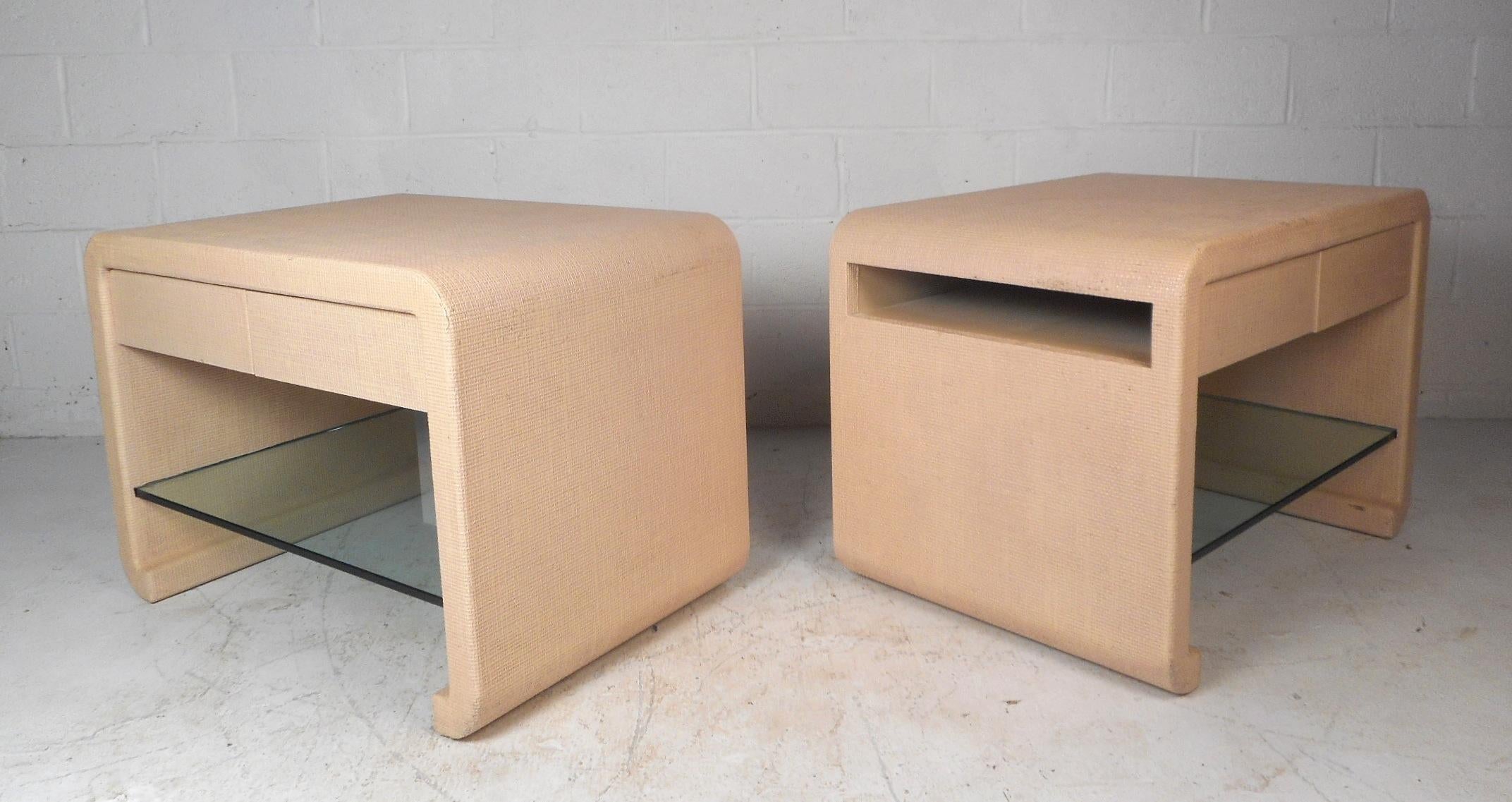 A unique vintage modern pair of night stands in the style of Karl Springer with drawers, side compartments, and thick glass shelves. The sleek waterfall shape covered in grasscloth offers a stylish and convenient place to set and store items. This