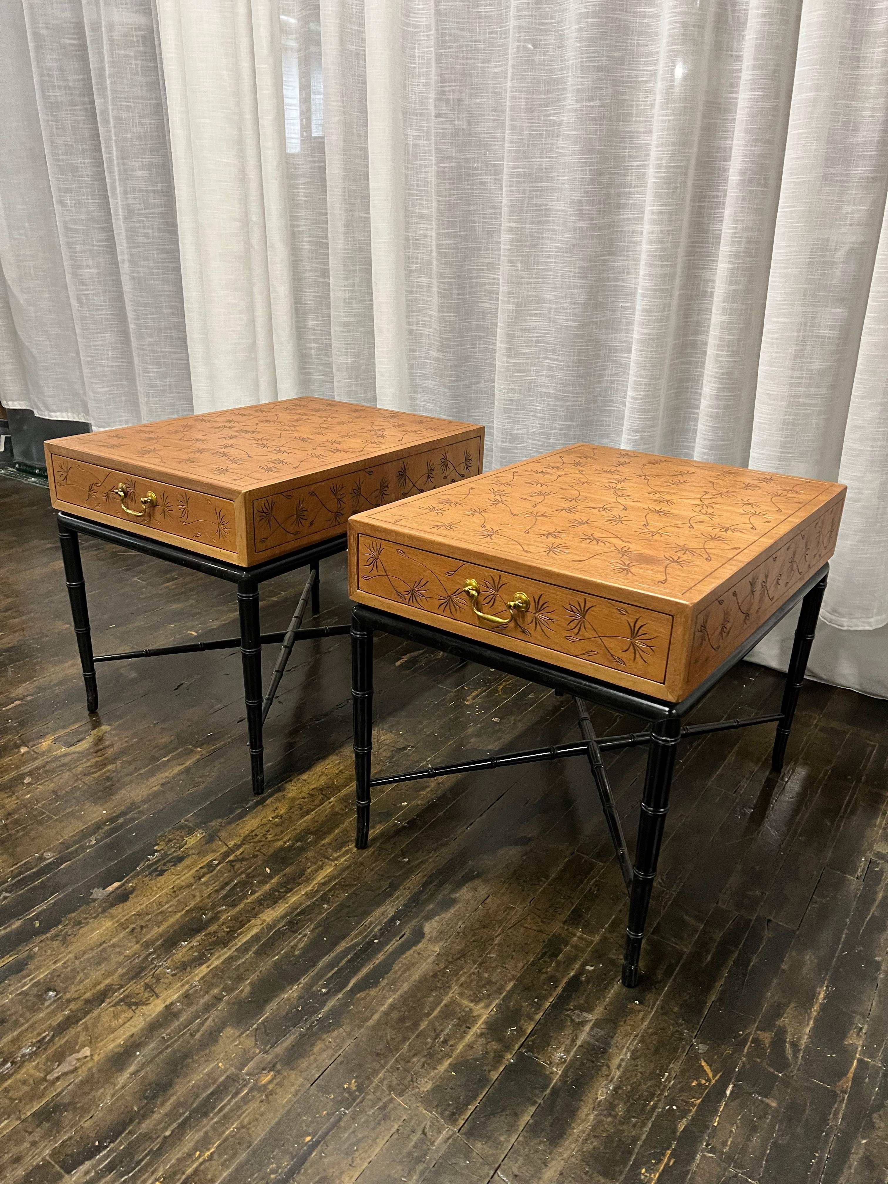 Lovely pair of Hollywood Regency style end / side tables with a walnut case that has an incised dandelion pattern (in black) and a single drawer with a brass drawer pull. The case rests on a black lacquered faux bamboo base with four tapered legs