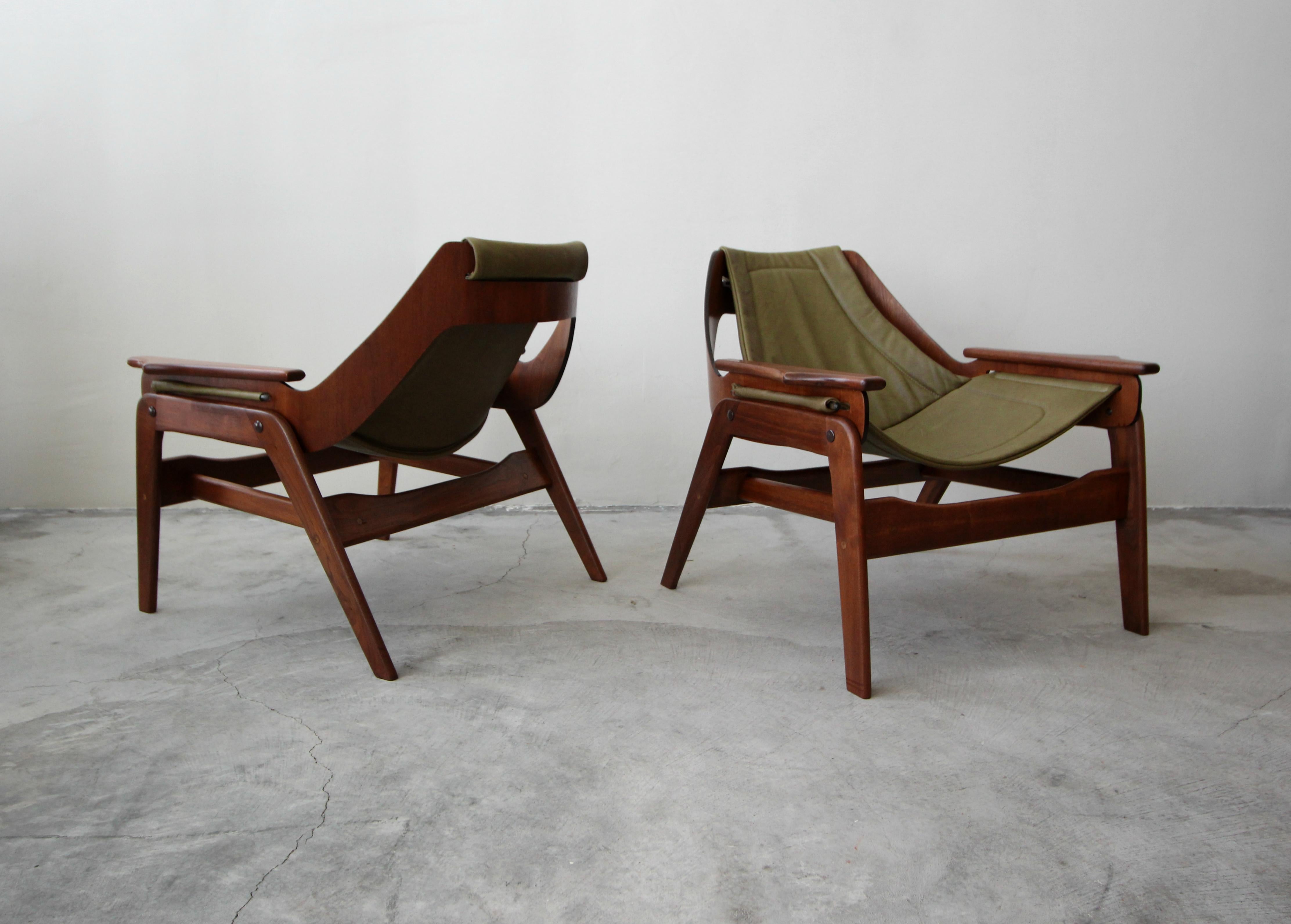 Beautiful pair of midcentury walnut and leather sling chairs by Jerry Johnson. The chairs feature beautiful sculptural frames and newly upholstered olive green slings. These chairs are the epitome of midcentury seating. More like art than chairs