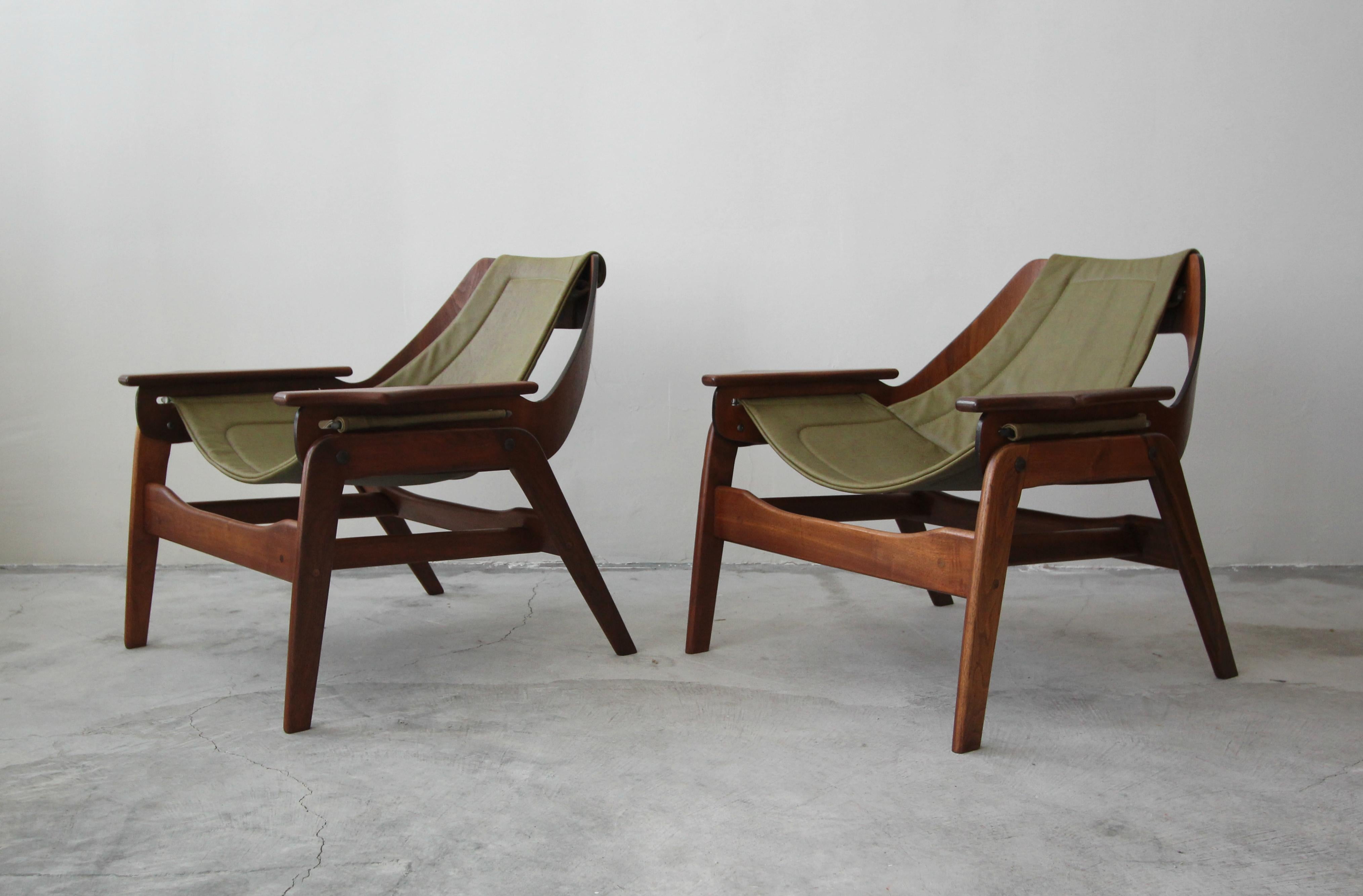 Beautiful pair of midcentury walnut and leather sling chairs by Jerry Johnson. The chairs feature beautiful sculptural frames and newly upholstered olive green leather slings. These chairs are the epitome of midcentury seating. More like art than